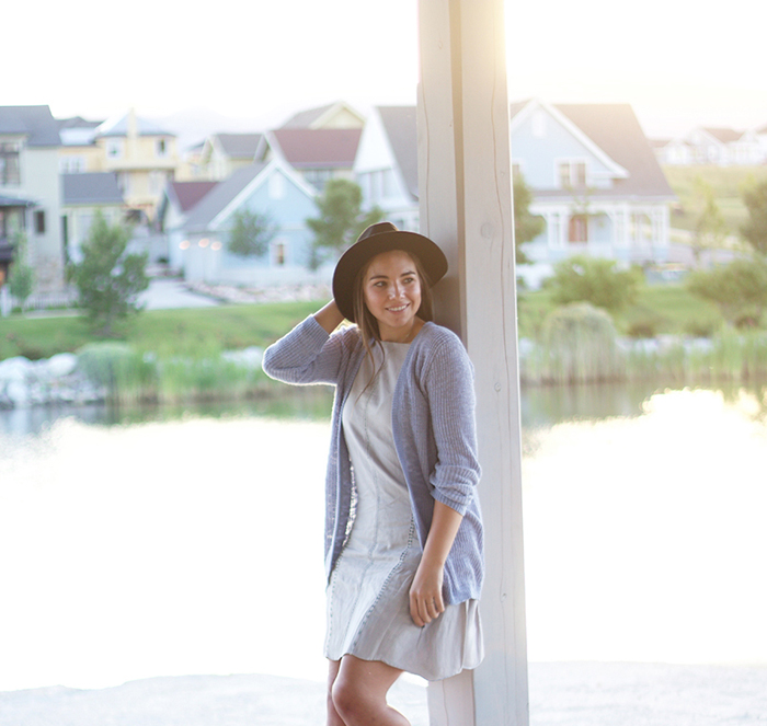 Lauryncakes standing on a dock wearing a greay dress, blue cardigan, and hat | How to thrift and find used clothing