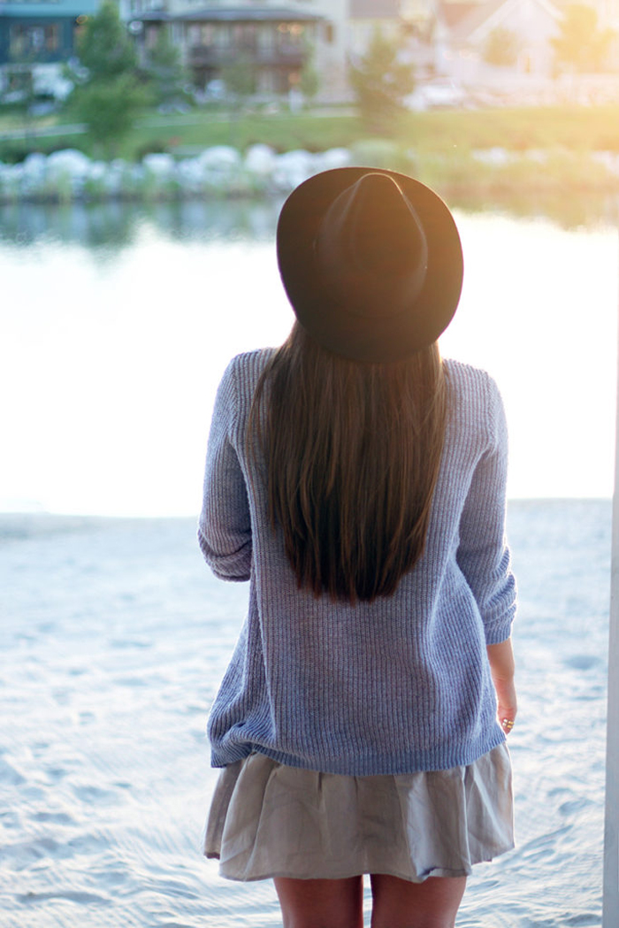 Woman looking out at a lake near sunset. SHe is wearing a dress, cardigan, and hat