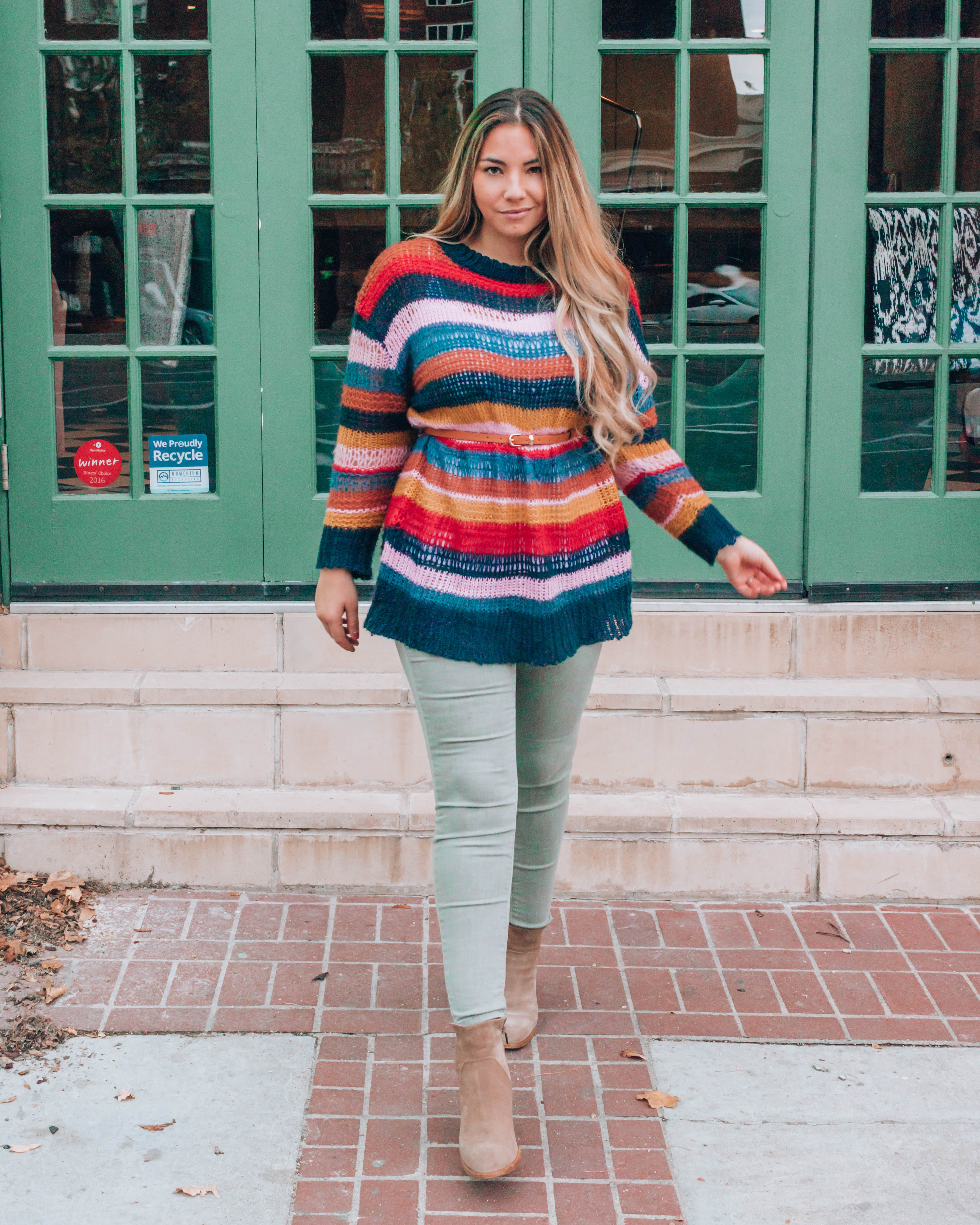 Blonde woman walking in striped sweater, green pants, and boots