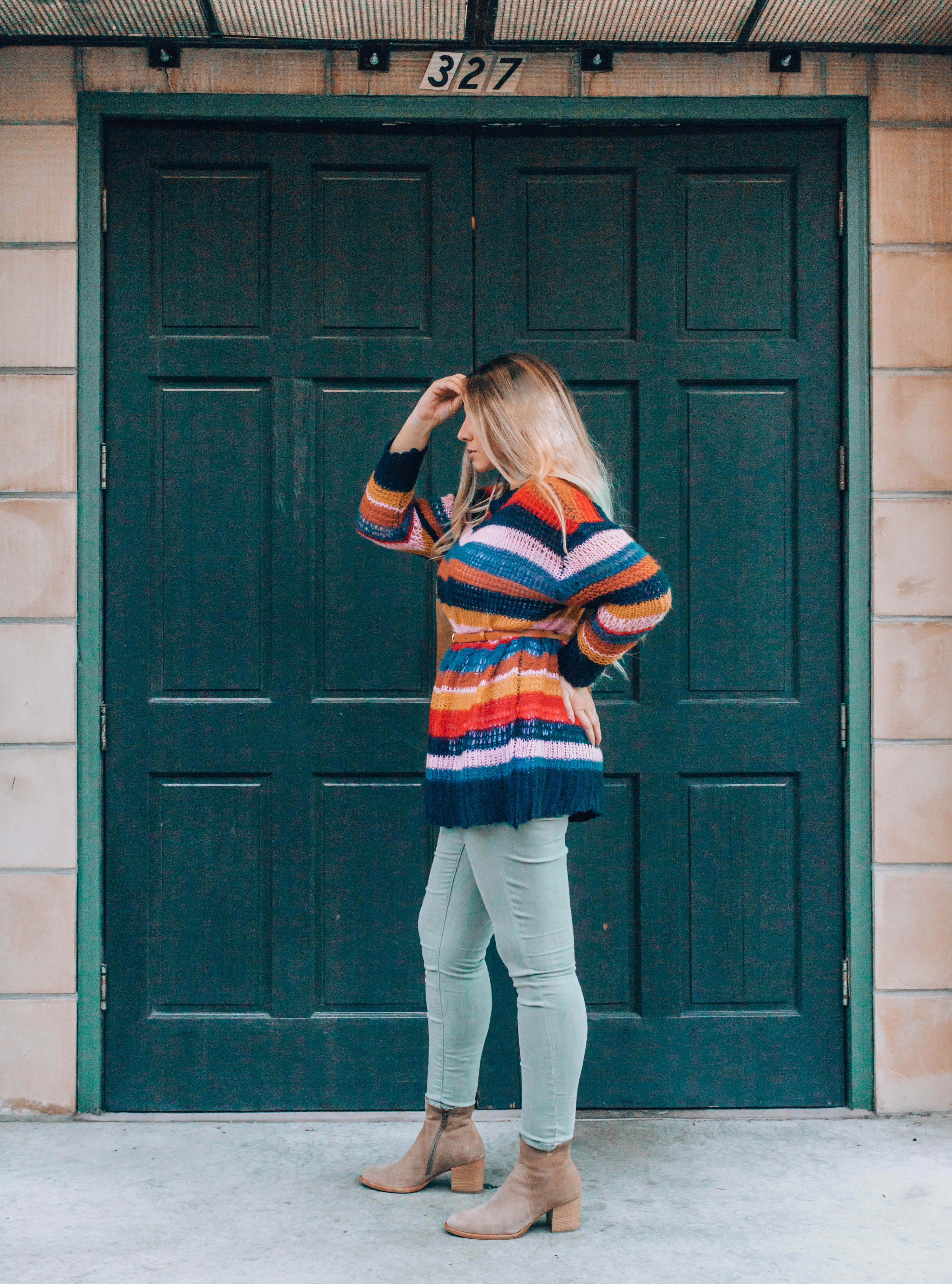 Blonde lady in sweater standing in front of a green door outside.