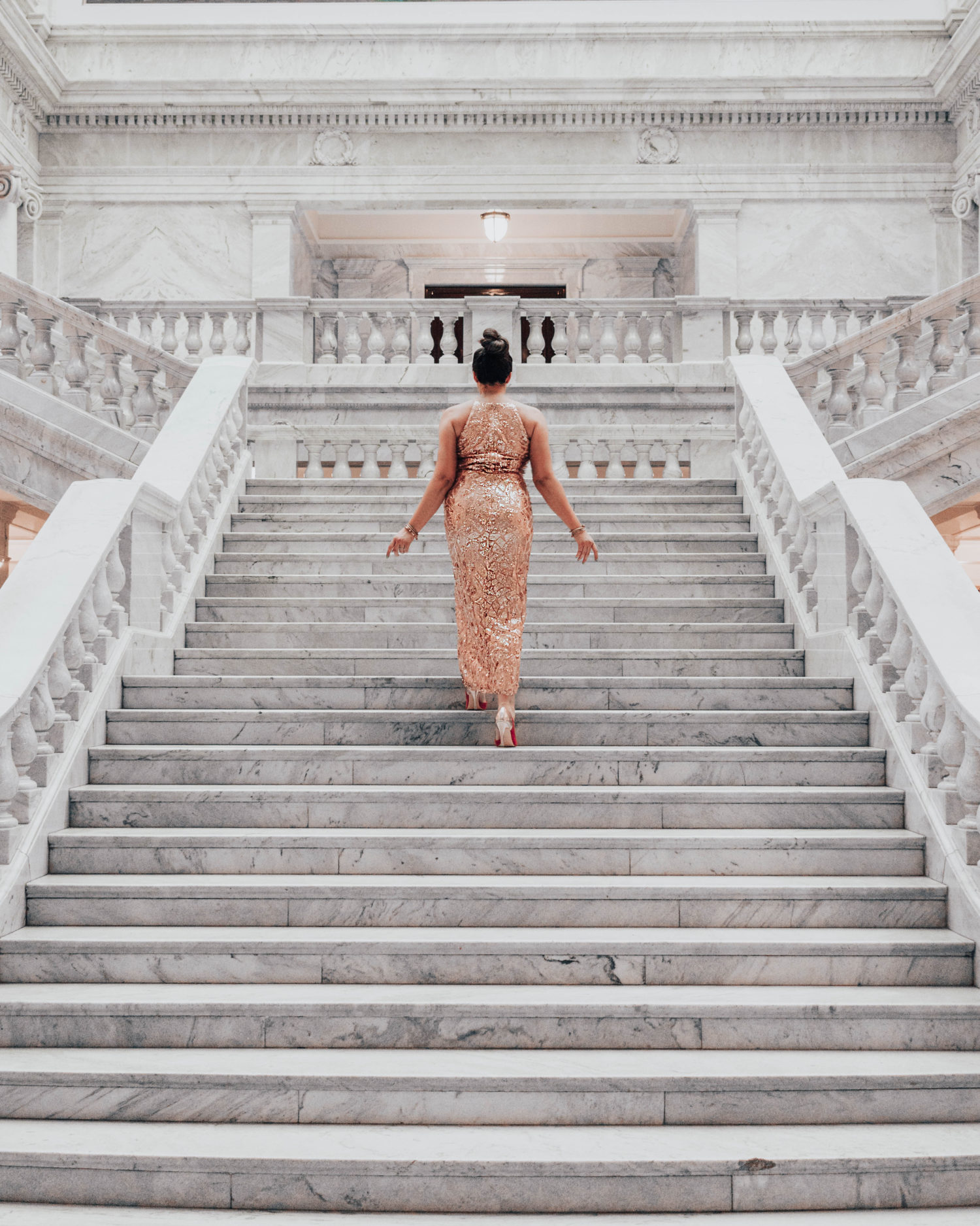 Woman in gold sequin dress walking up large marble staircase