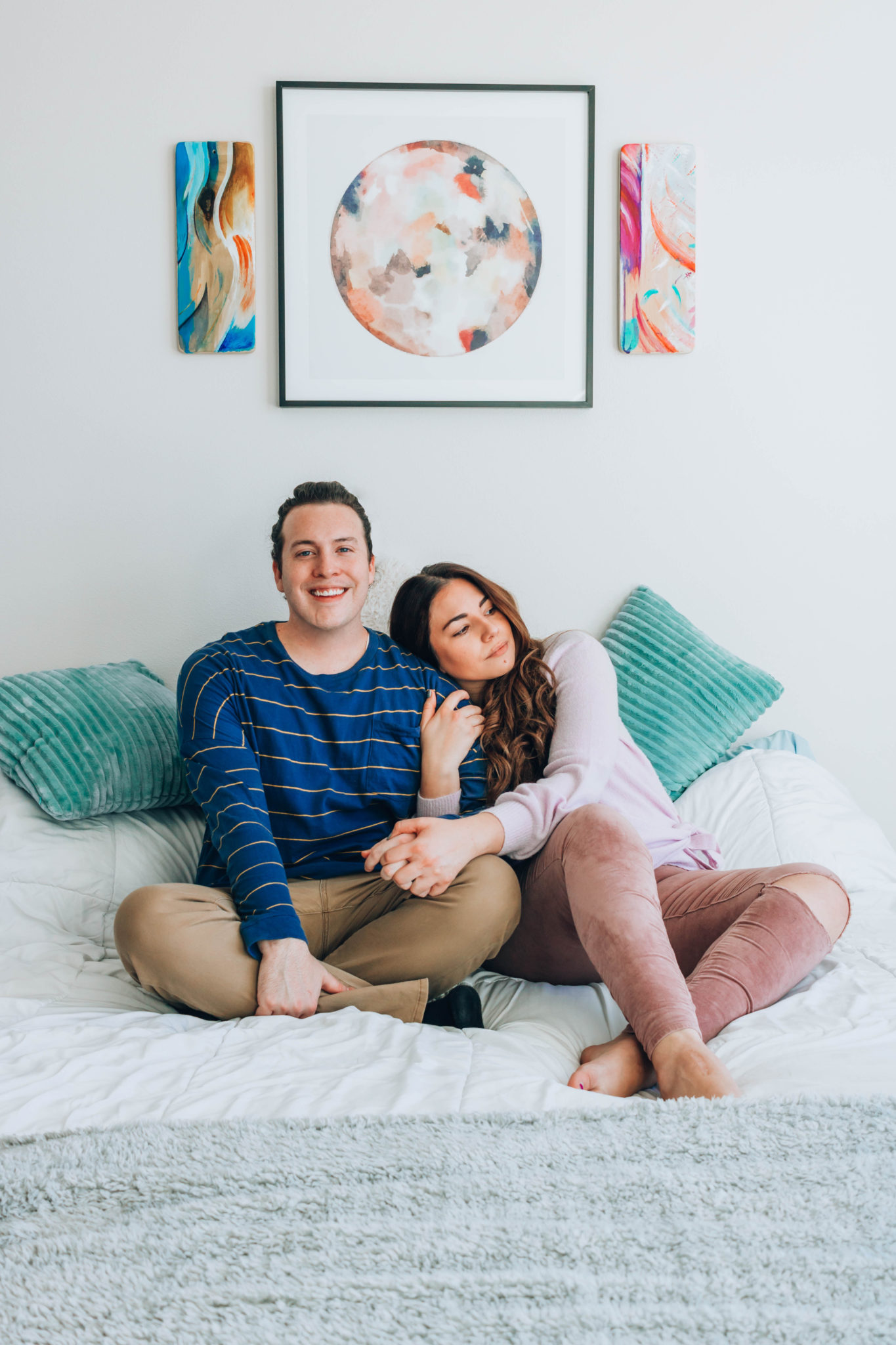 Couple seated on their bed beneath their spirit paintings.