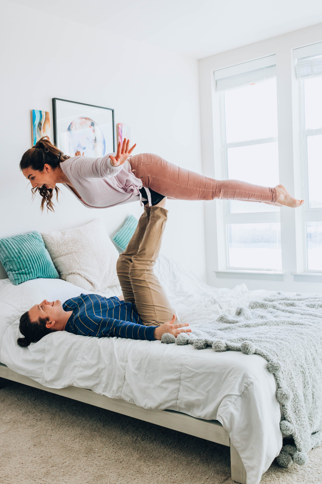 Couple playing airplane on their bed in front of their spirit paintings.