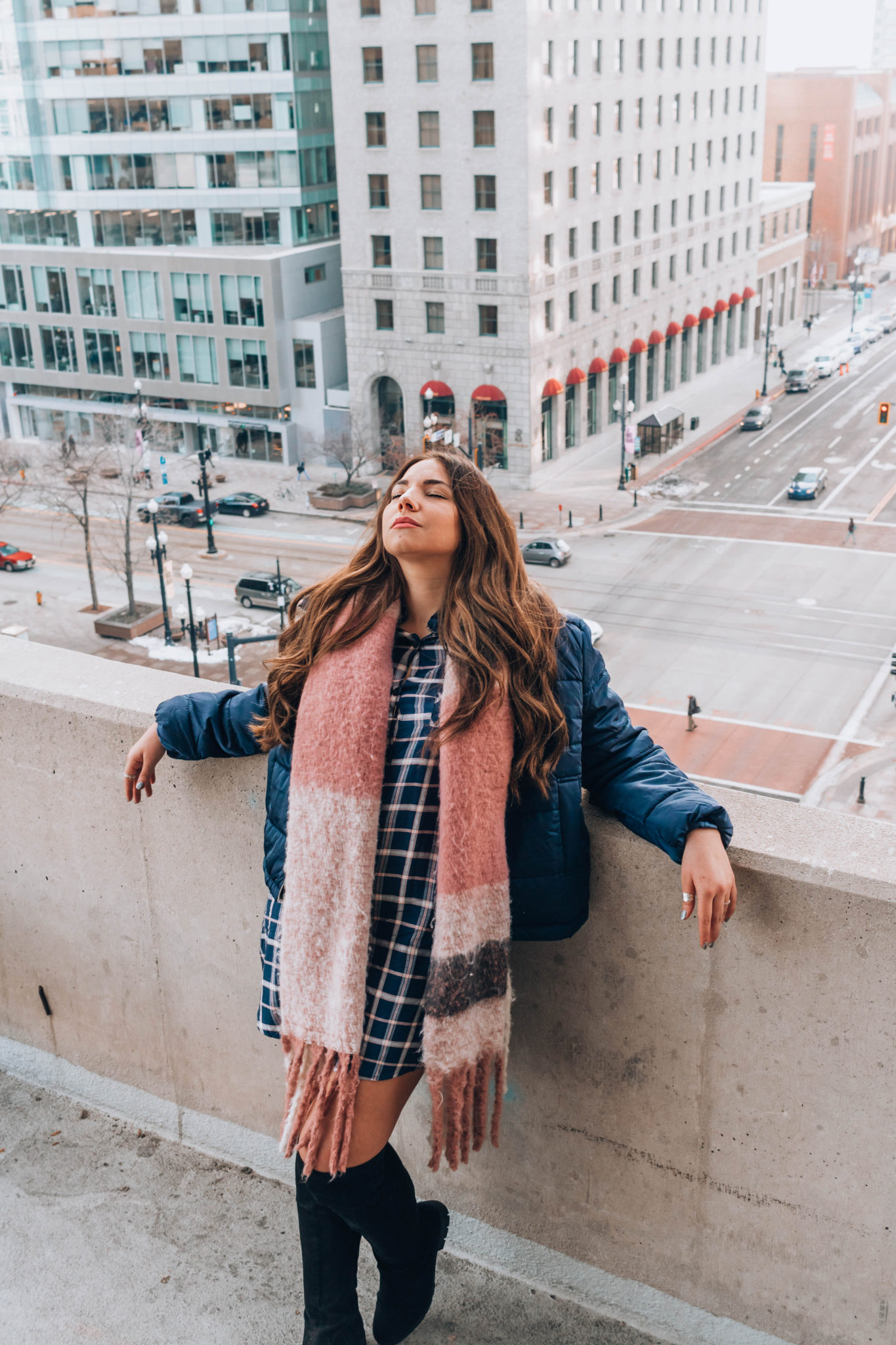 Brunette fashion blogger leans against rooftop rail above Salt Lake City skyline.