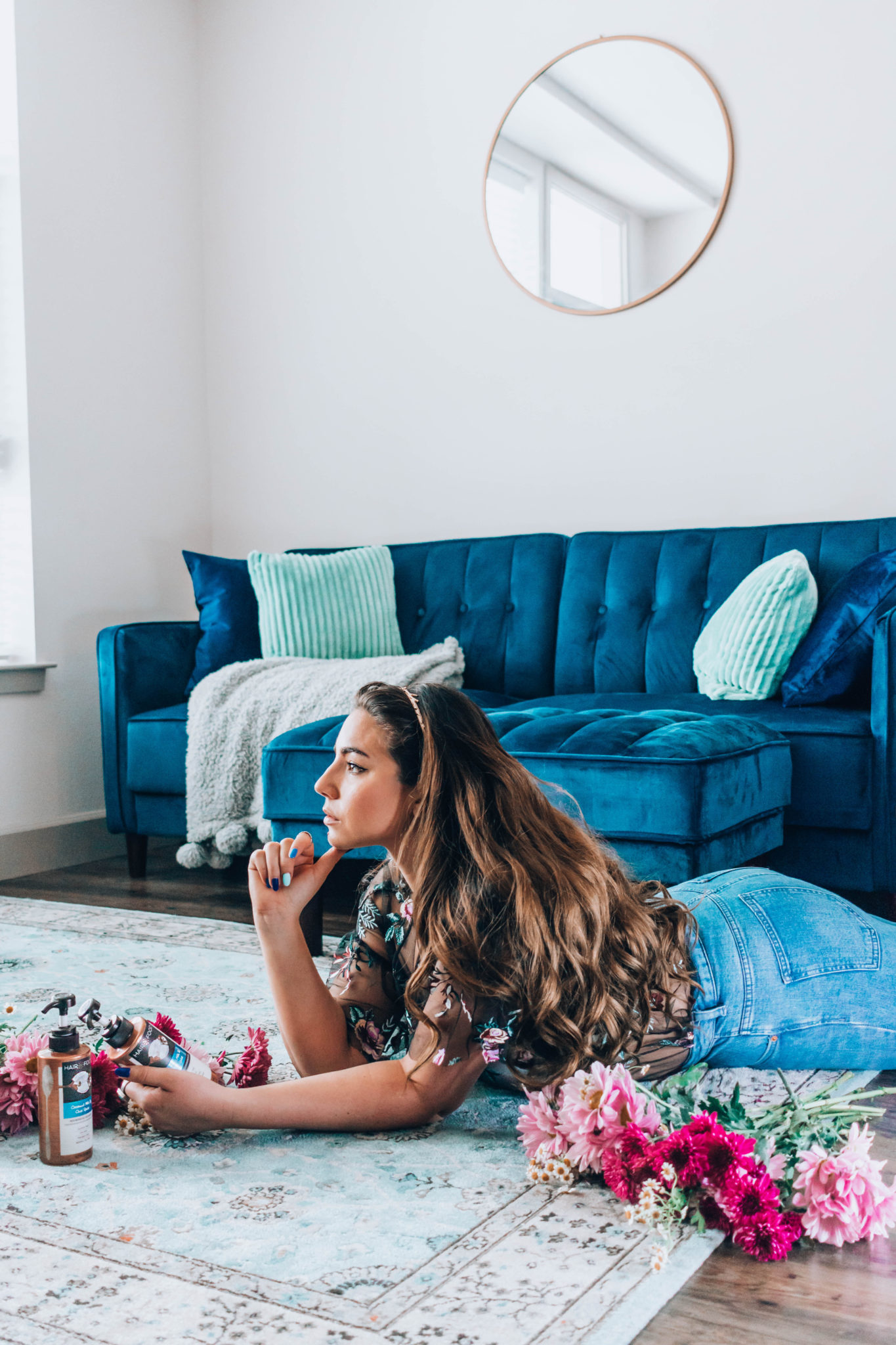 Lauryn Hock sitting on her stomach in the living room surrounded by her blue couch and pink flowers holding Hair Food shampoo and conditioner.