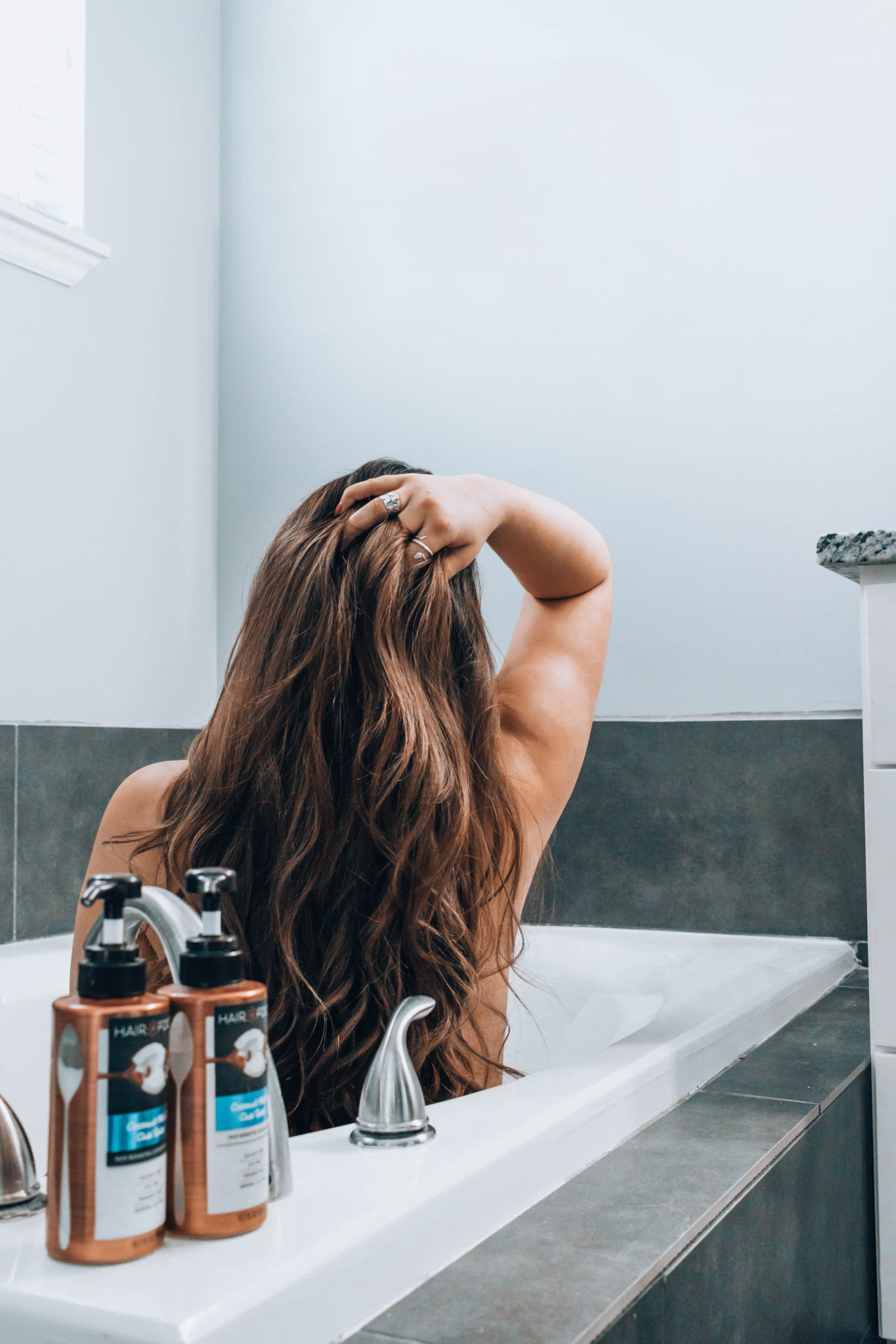 Women with thick, curly, long hair sitting in a bathtub with shampoo and conditioner.