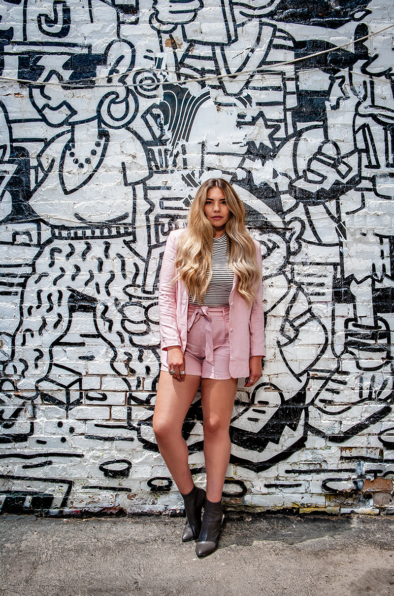 Social Media Influencer posing in a pink outfit in front of a painted wall. 
