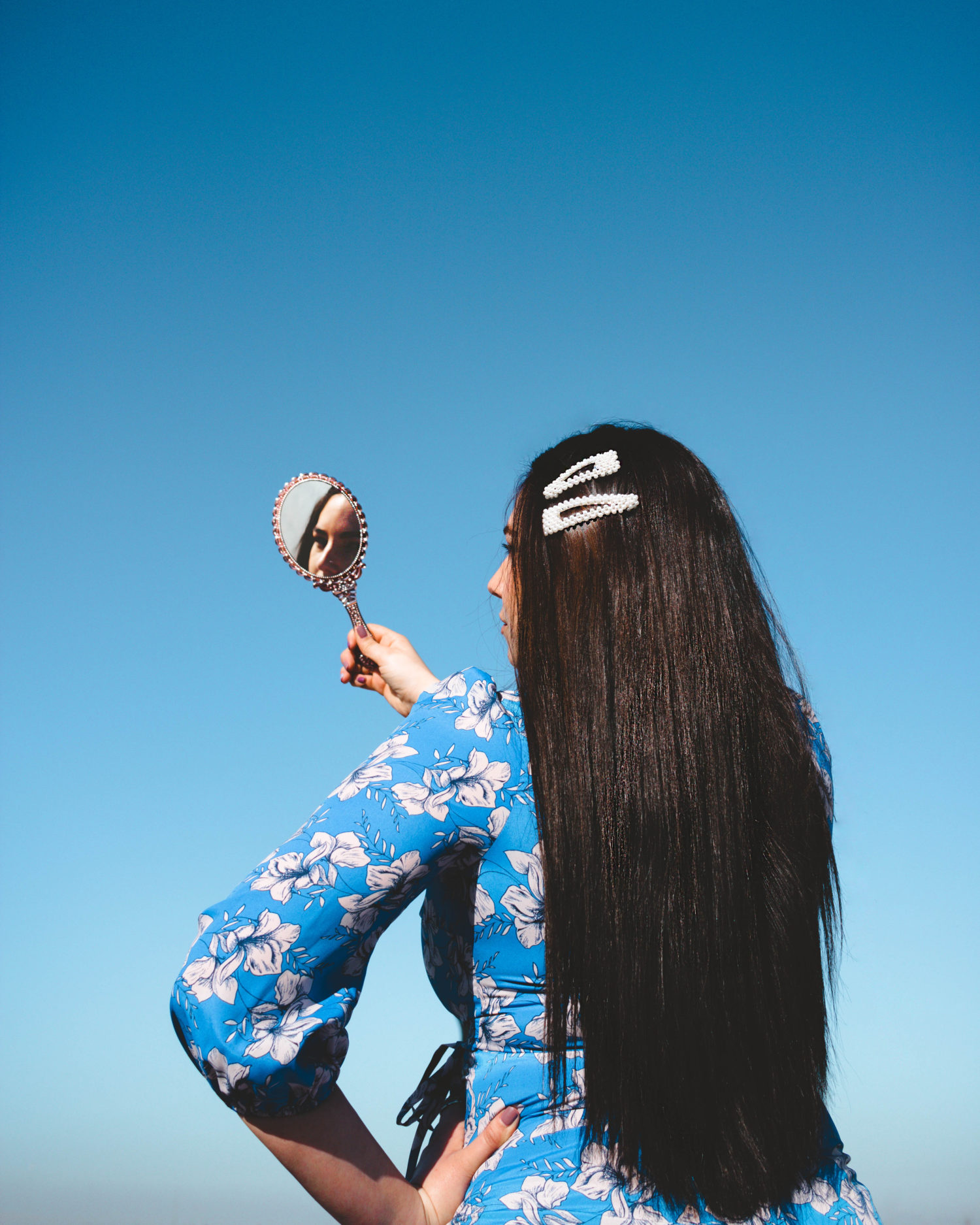 Lauryn Hock from Lauryncakes with long, straight, black hair looking into a mirror with a blue sky as the background.