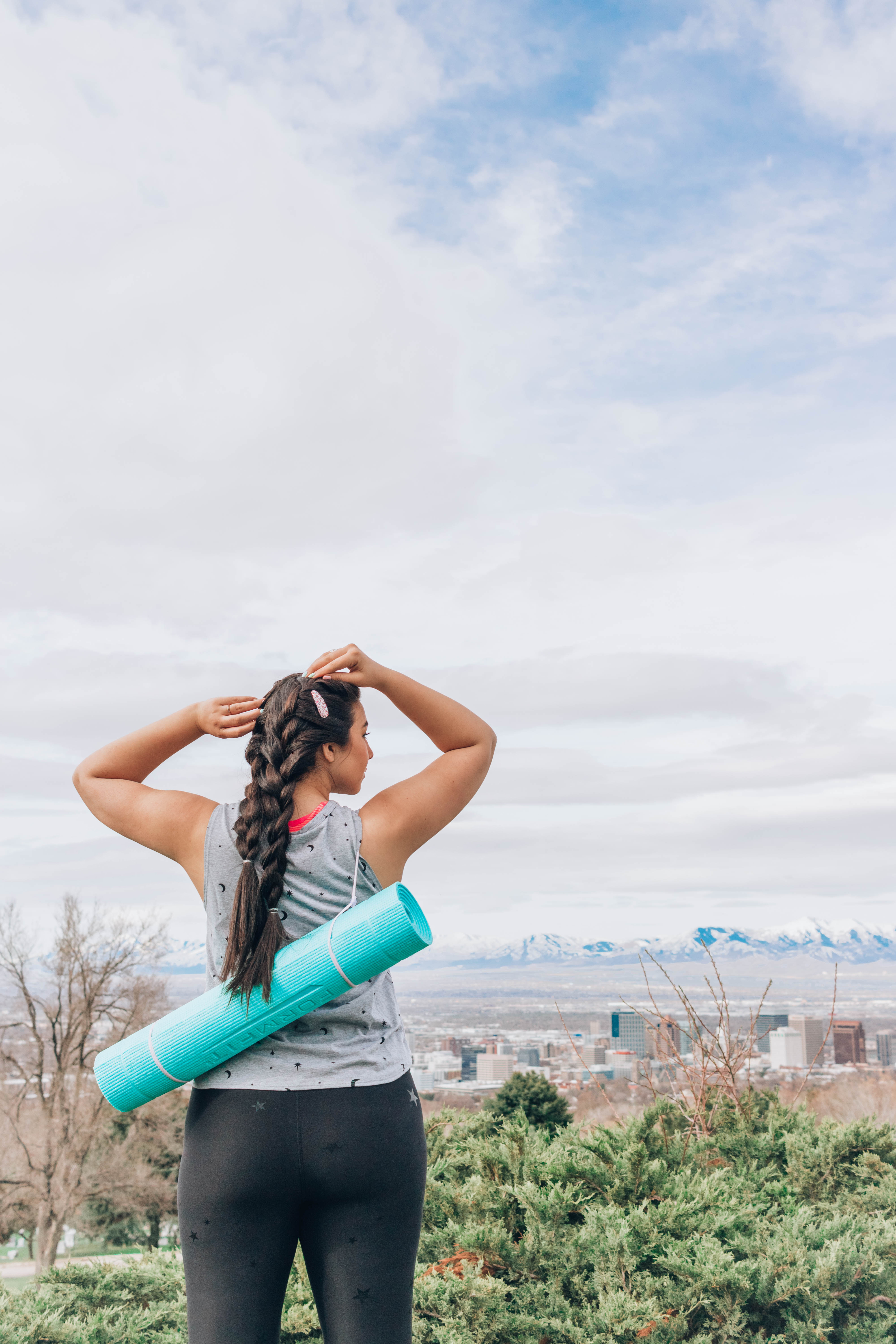 Lauryn Hock holding a yoga mat while looking at Downtown Salt Lake City from a park view