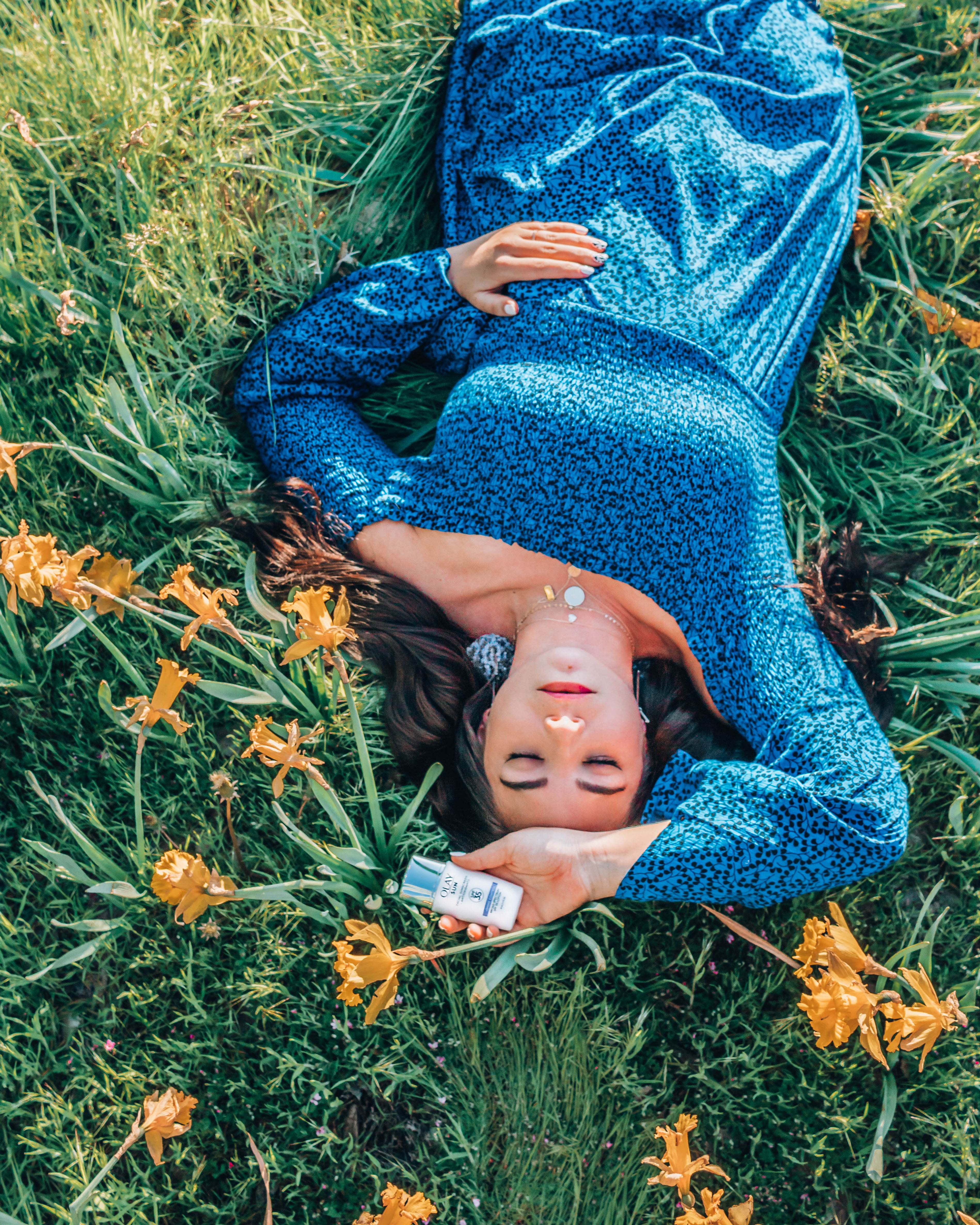 Woman in a blue dress and big earrings laying in a bed of daffodils.