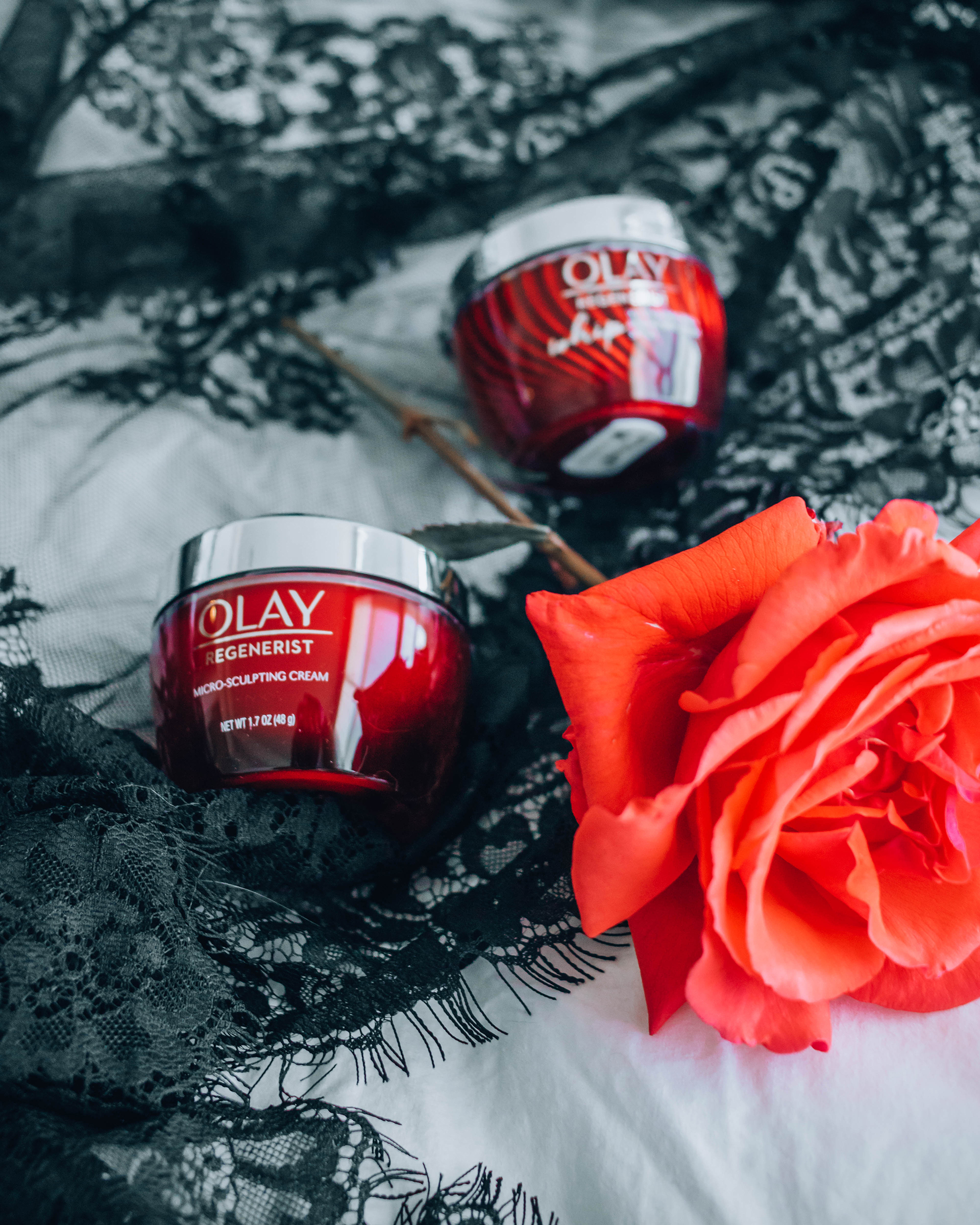 Olay red jar skincare bottles laying on a lace shawl next to a rose