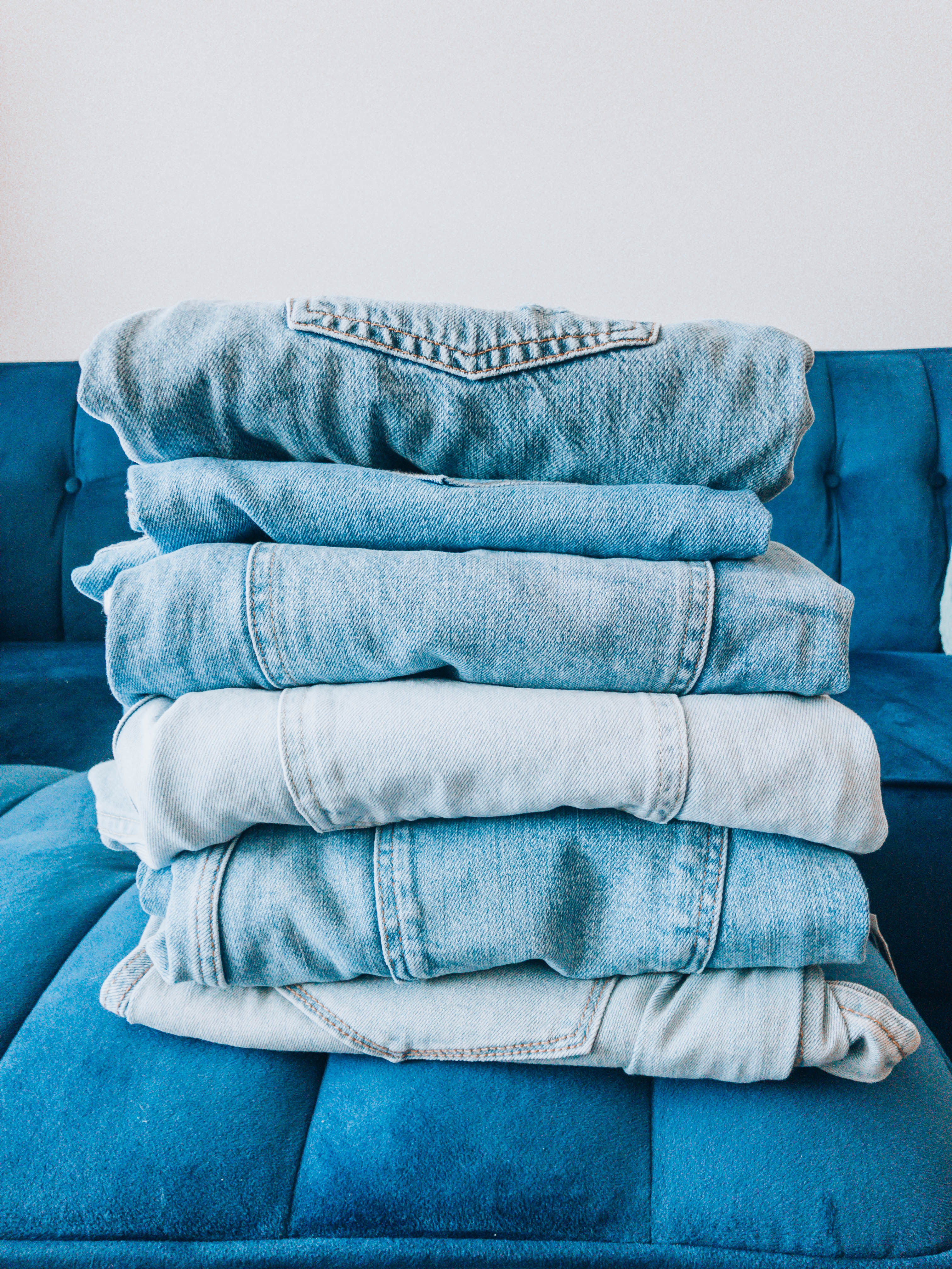 A stack of jeans sitting on a blue velvet couch