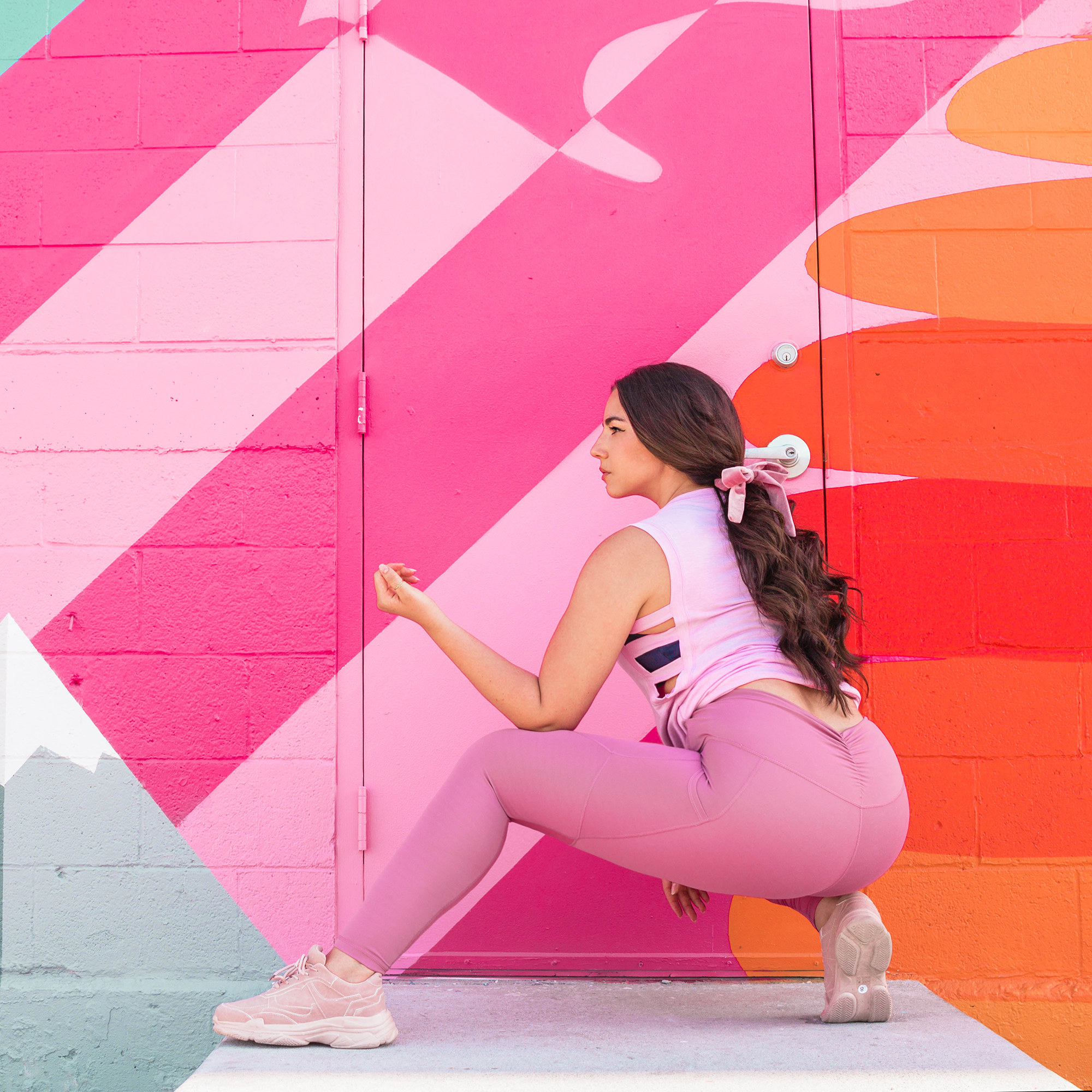 Lauryncakes with her hair in a curly pointail with a ribbon wearing workout clothes in front of a Slat Lake CIty, Utah mural