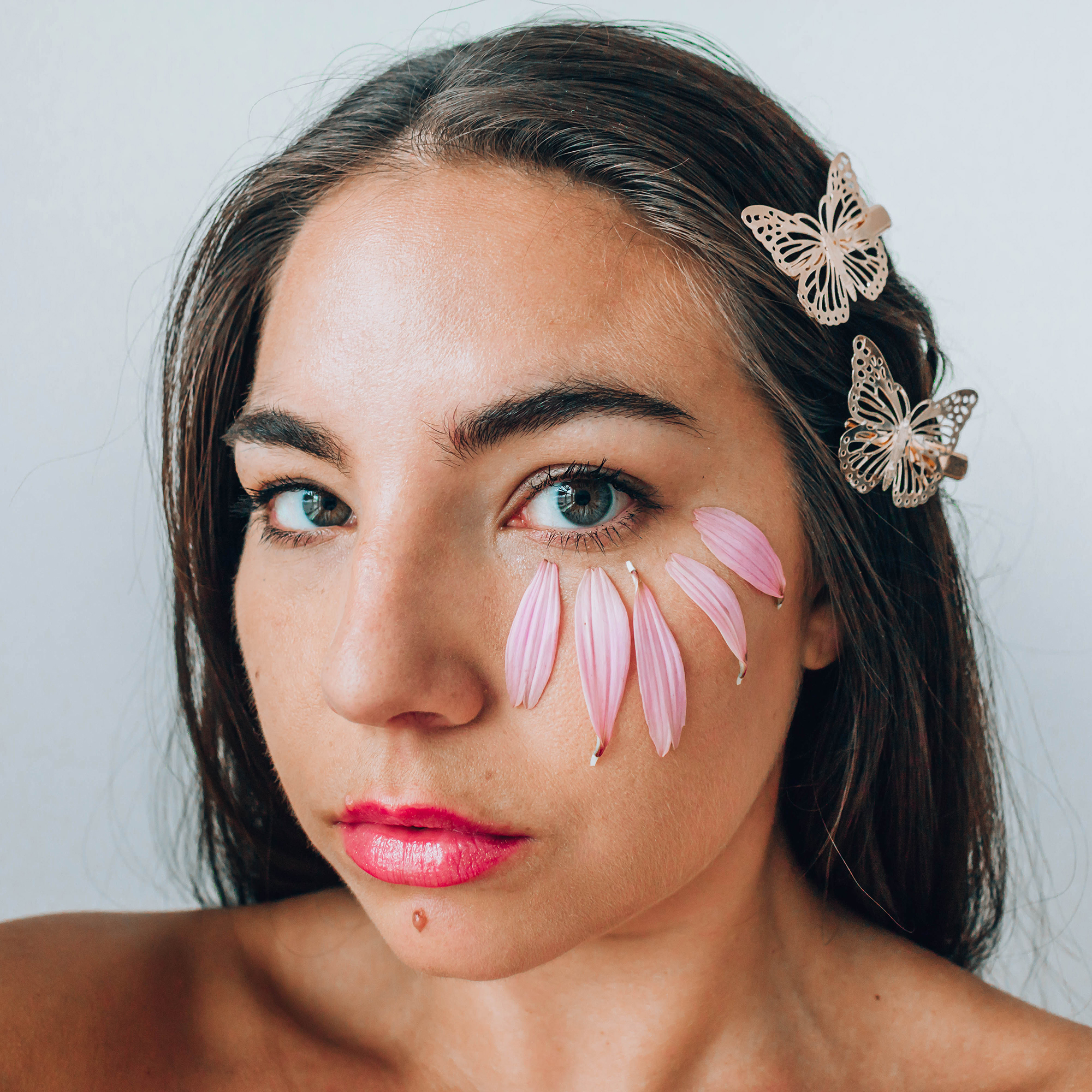 Close up portrait of Lauryncake's (Lauryn Hock) face with butterfly clips in her hair and flower petals under her eyes