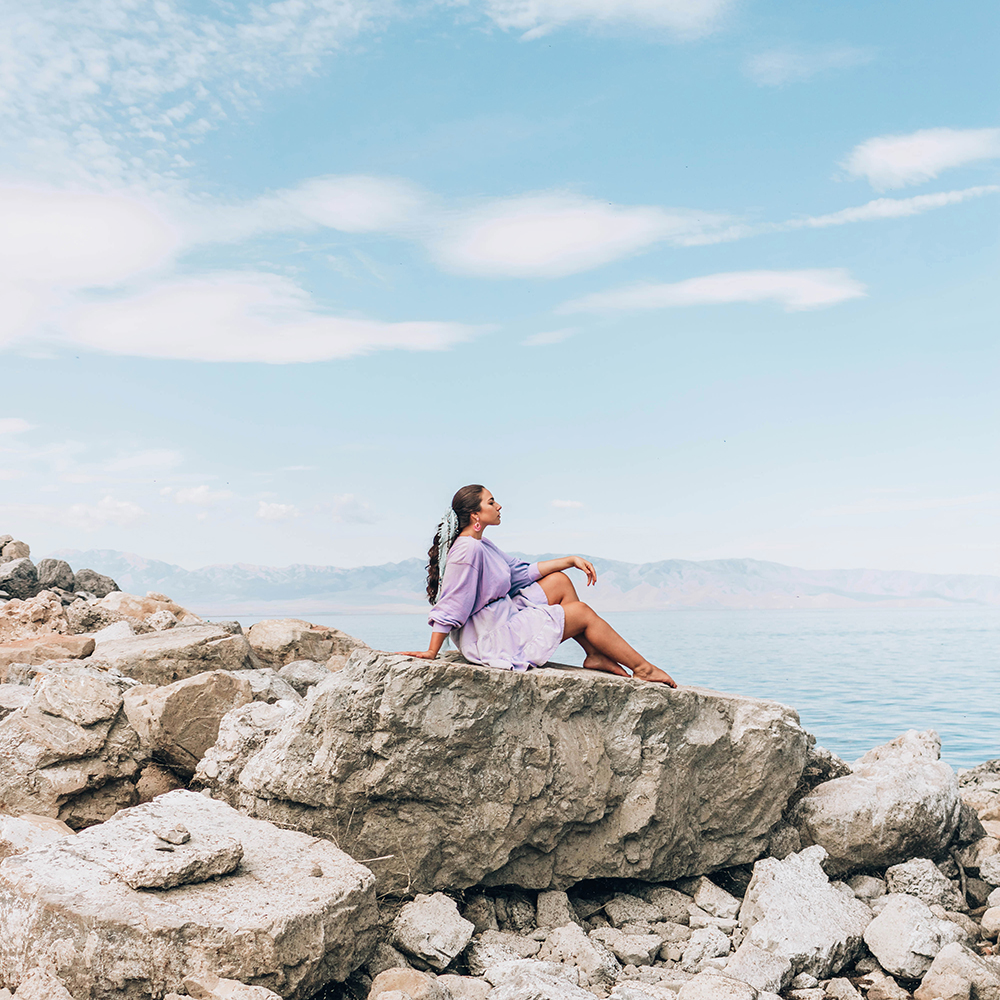 Lauryncakes (Lauryn Hock) sitting on a white granite rock at the Great Salt Lake. She is wearing a purple Free People dress and has a blue Madewell scarf tied around her hair.