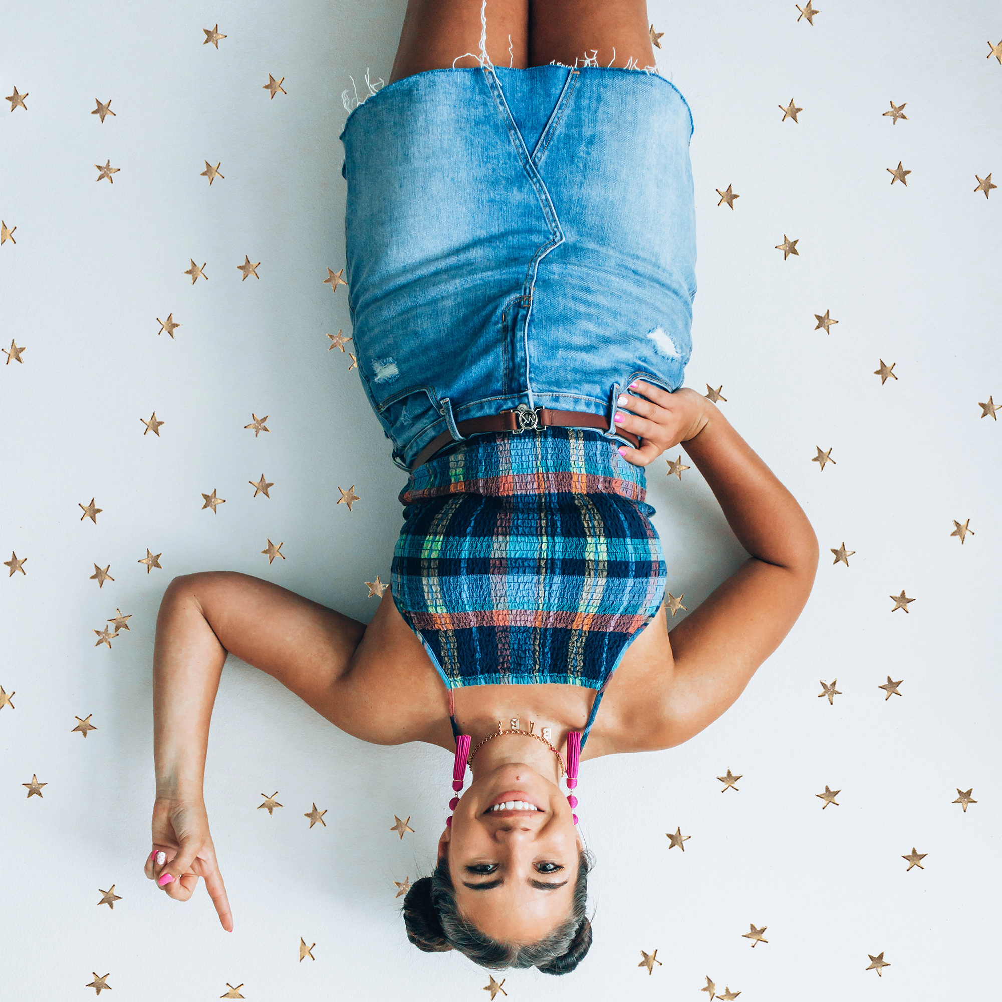 Upside down photo of Lauryn pointing in the air. There are gold stars on the white wall