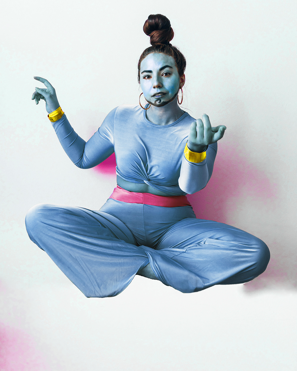 Lauryn Hock from Lauryncakes is dressed as Genie from Aladdin in head to to toe blue silk. She is floating in the air while her hair is in a bun on top of her head and she has a beard drawn on her face.