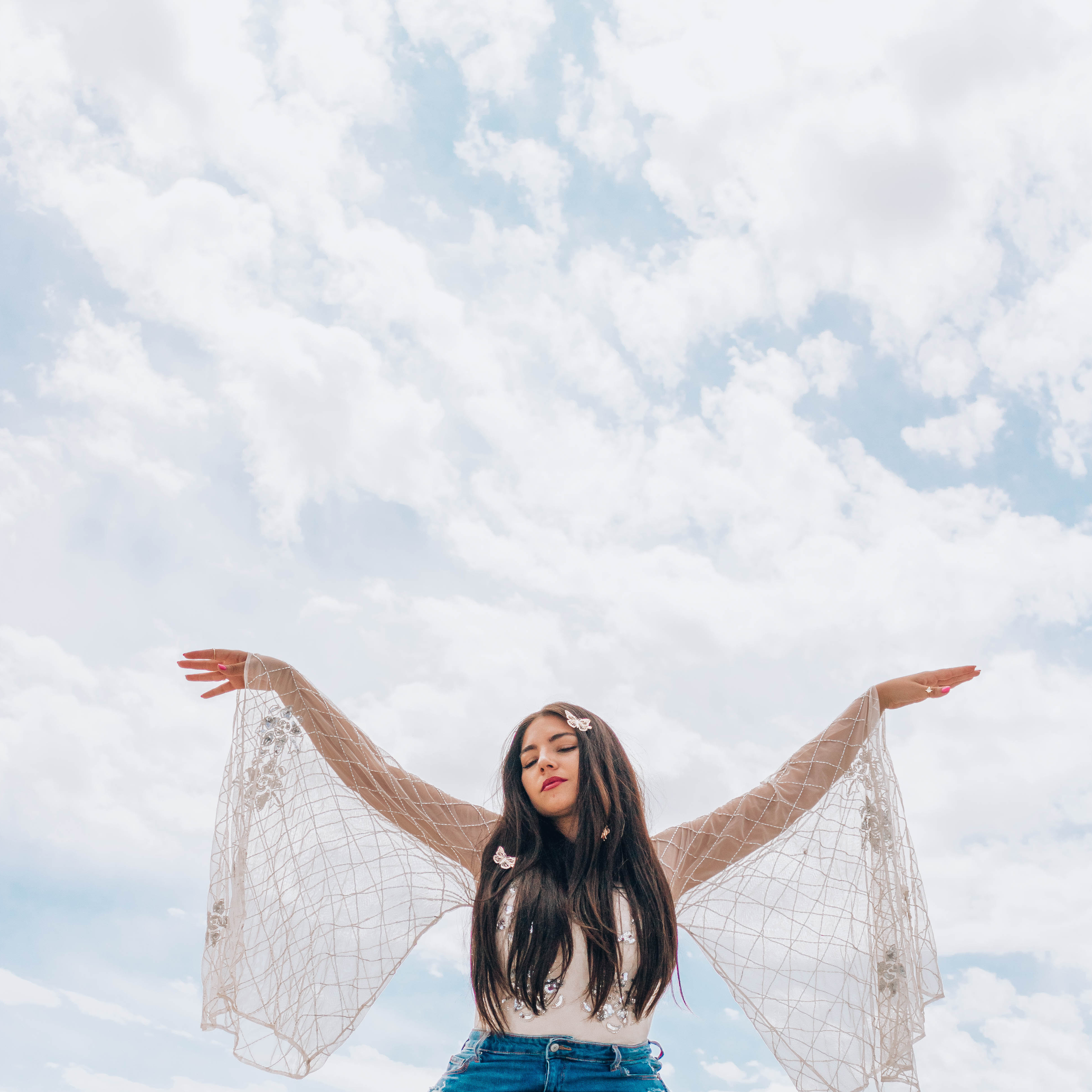 Lauryn from Lauryncakes has her arms spread high in the air like wings while a blue sky with clouds sits behind her. In this post, you will find Vitamin C products that will brighten your skin.