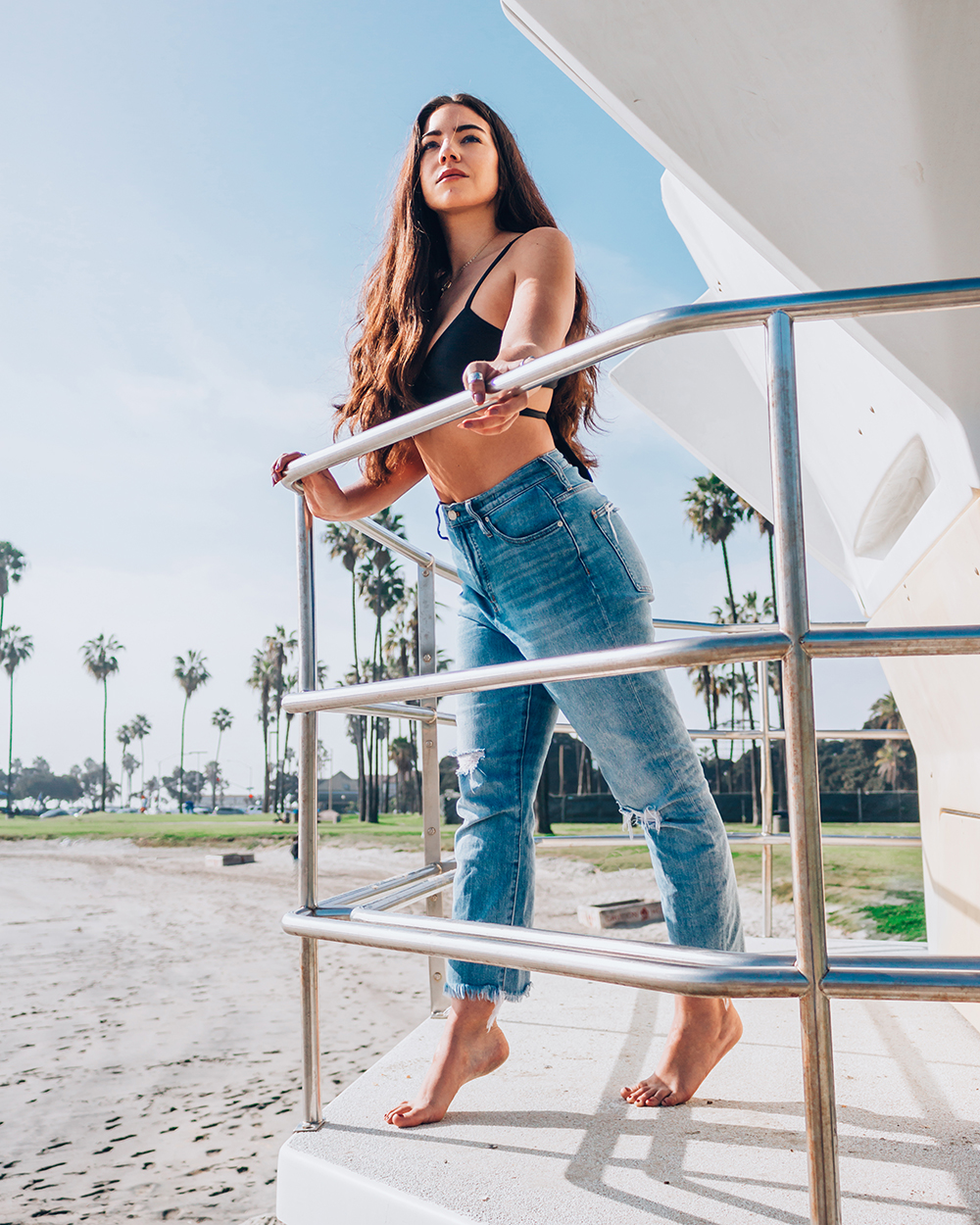 Lauryncakes leans over the railing at a lifegaurd tower in Mission Beachl Sandiego. She is wearing mom jeans and a bikini top