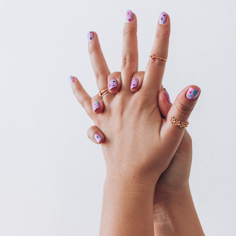 At-home manicure of purple matte nail polish with blue, pink, and green polka dots on top