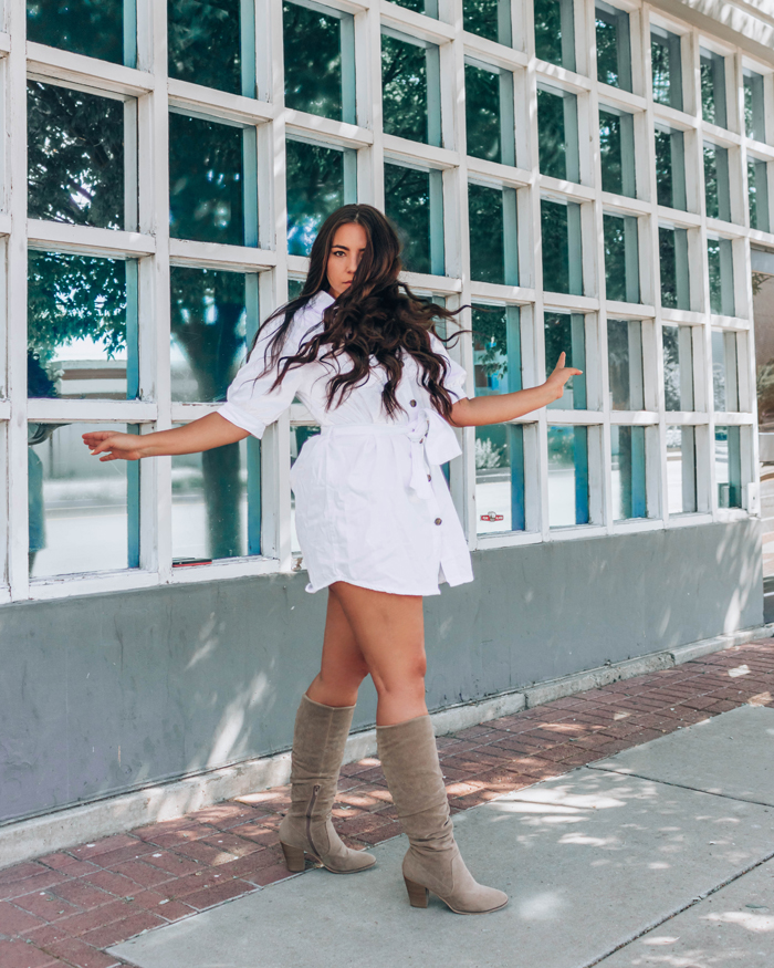 LAuryn Hock of Lauryncakes spins towards the camera while wearing knee-high slouchy boots and a white mini dress with a tie around her waist. Her long, brunette hair is down.  |  | Fall Fashion Trends 2020