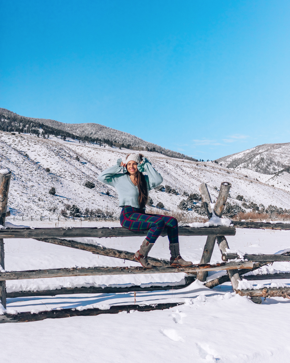 Utah blogger, Lauryncakes, sits on a fence in a Utah field covered in snow