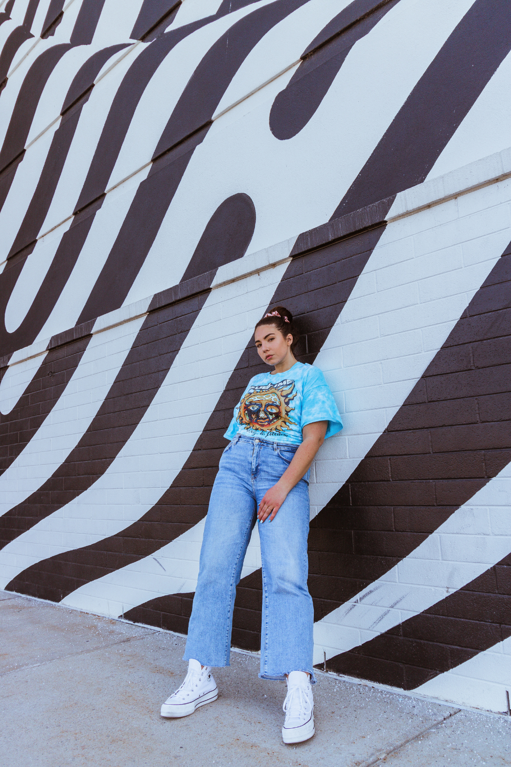 A white and black striped mural in Salt Lake City is behind influencer Lauryncakes as she poses in converse, wide leg jeans, and a band tshirt for her Spring outfit