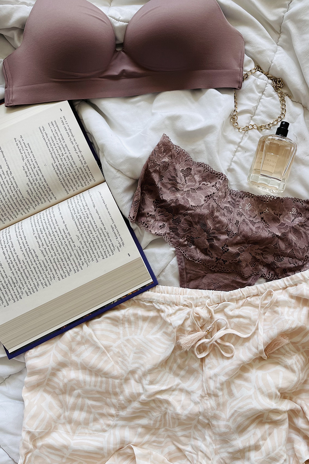 packing for a trip | intimate wear, shorts, a book, and perfume on a bed