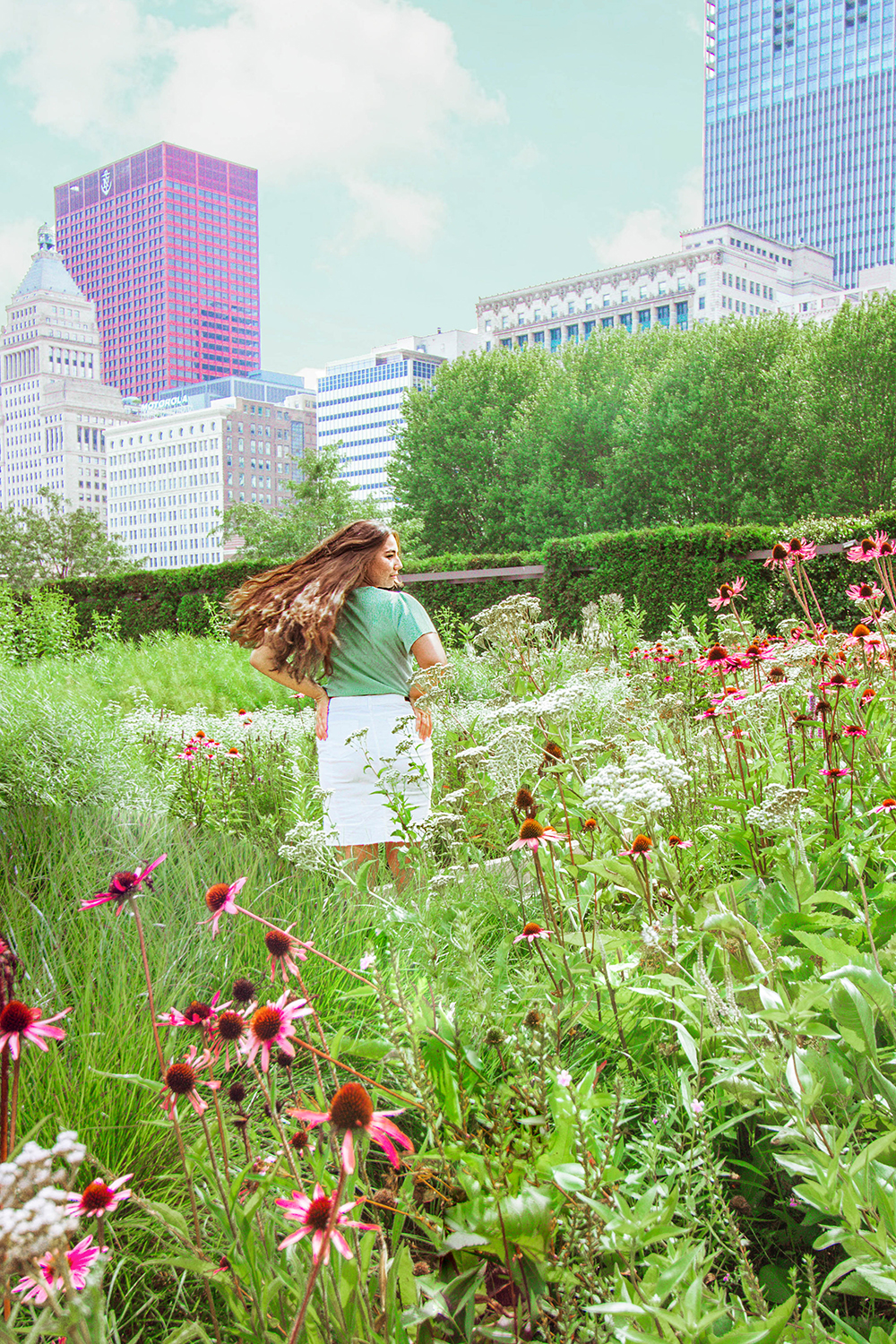 Midsize fashion and style blogger flips her hair in Lurie Garden near flowers with the cityscape behind her