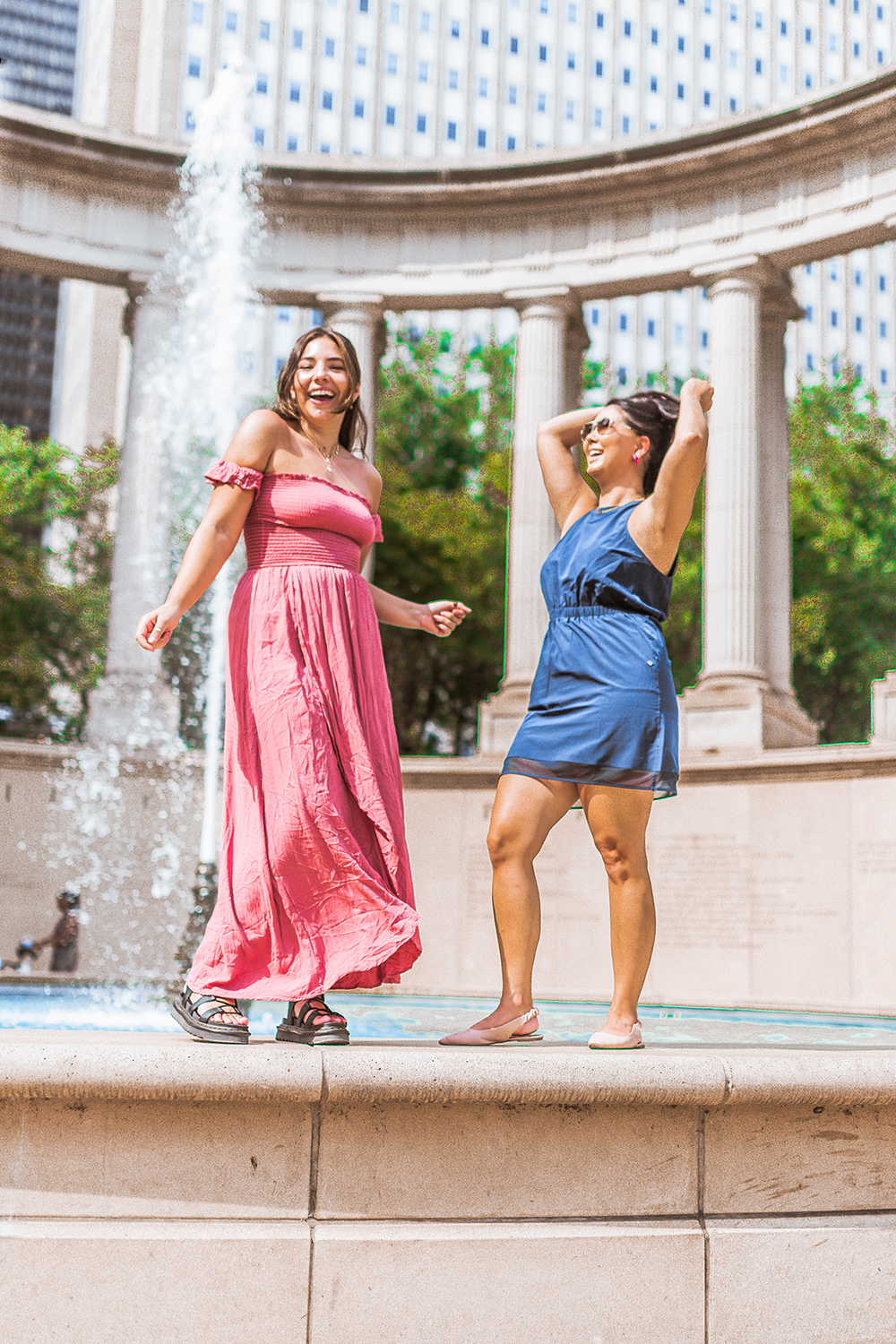 two wwomen dance and smile on the ledge of a fountain at Millenium Park
