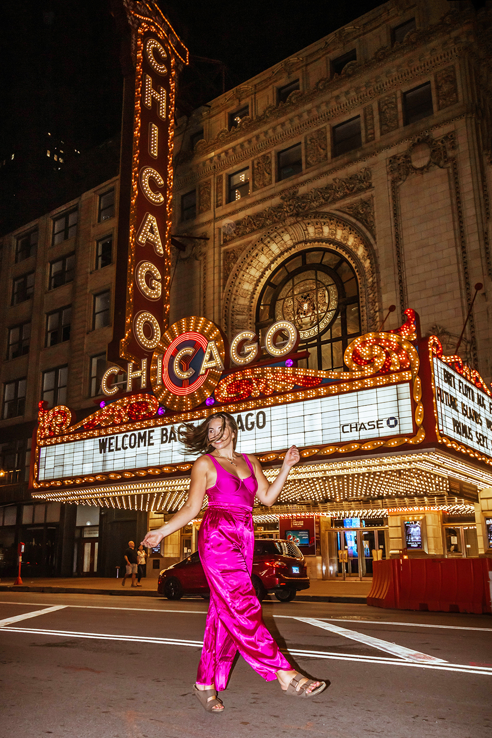 Nighttime photo of Lauryn walking in the street in front of the Chicago Threatre that has a lit up marquee