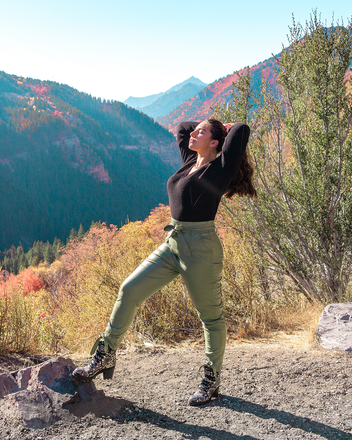 Lauryncakes, midsize style blogger, wearing colored faux leather pants, a knit sweater, and boots while standing near a canyon with changing fall leaves