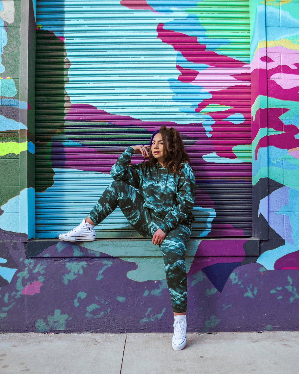 Instagram influencer Lauryncakes sits in front of a painted garage with a colorful wall mural while wearing a green sweat suit with camo print