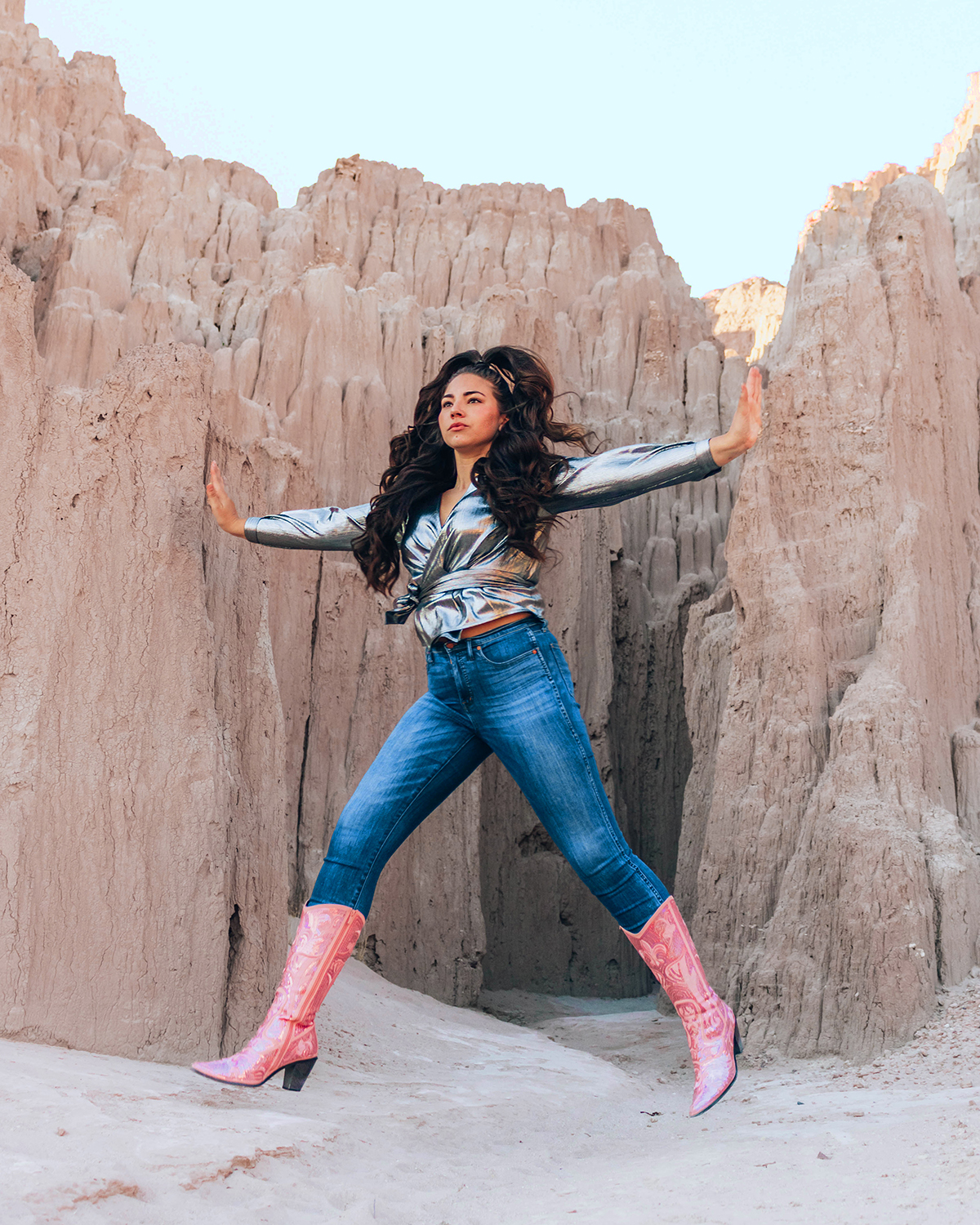 Lauryncakes jumps in to the air in front of Cathedral Gorge in Nevada while wearing sparkly boots, jeans, and a metallic blouse