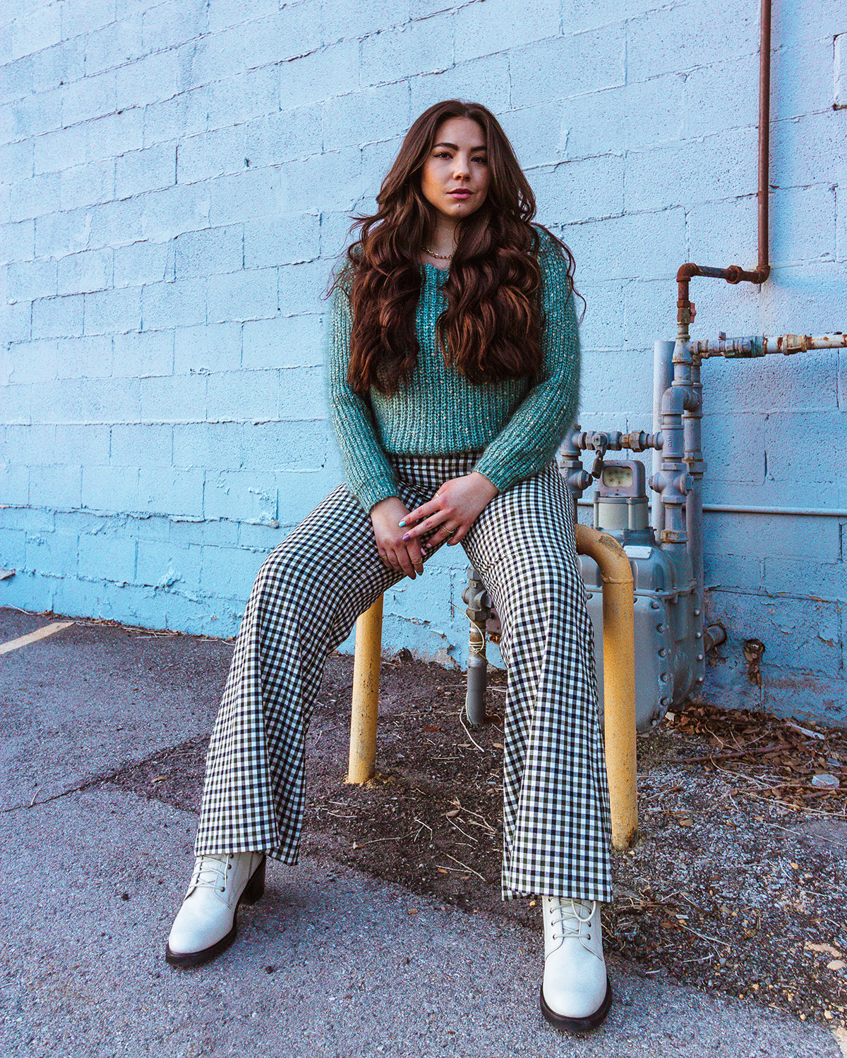 Lauryncakes sitting on a yellow pipe while wearing an oversized knit sweater and wide leg jeans