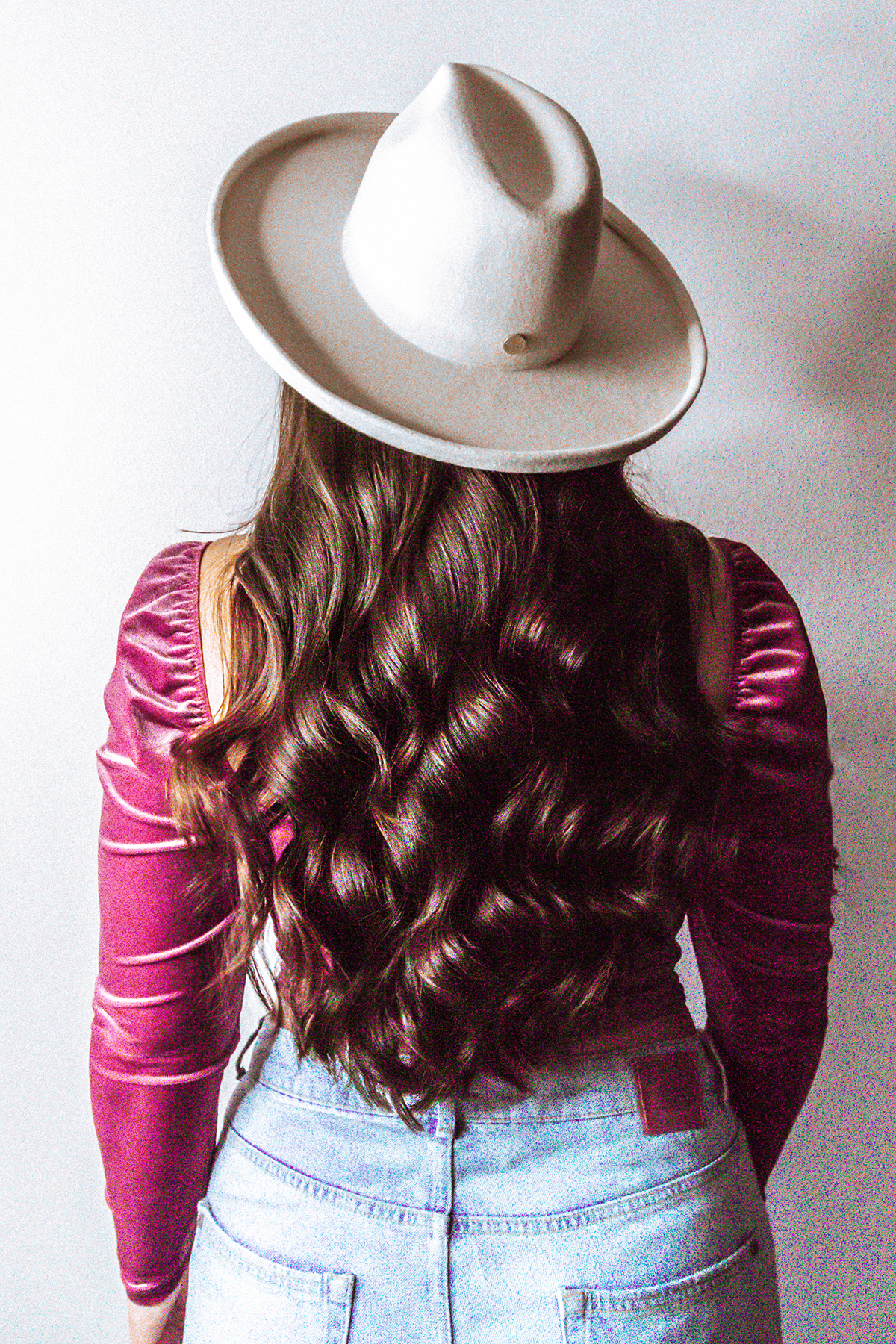 backside of a woman with long and thick brunette hair wearing a white wide brim felt hat, a velvet long sleeve top, and high waist jeans | shampoo tops