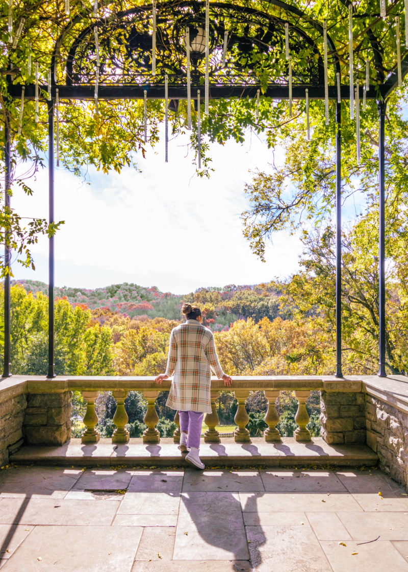 Lauryncakes walking through fall foliage atCheekwood Botanical Gardens in Nashville. Her thick hair is in a bun and she's wearing a long sleeve blouse with ruffle shoulders, barrel wide leg corduroy pants, and converse platform high top sneakers