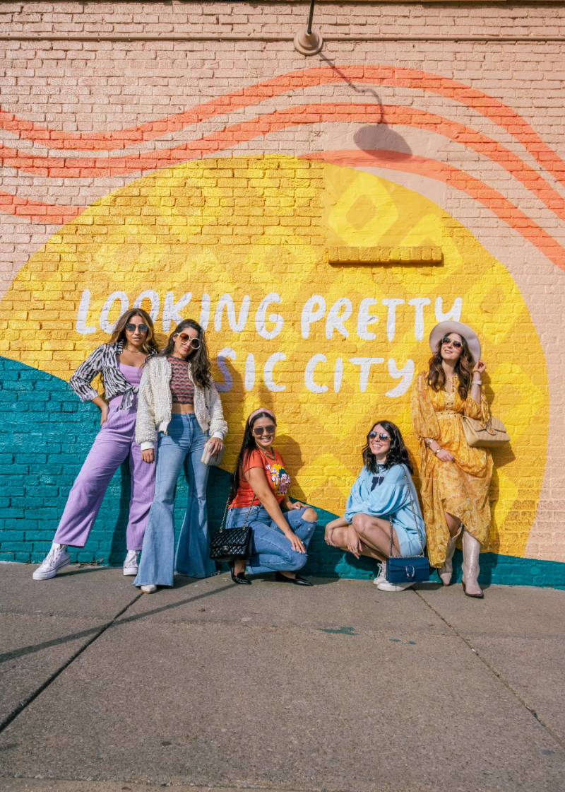 5 women from the Babes That Wander travel blogging group stand in front of a Nashville mural on a girls trip. The mural says, "looking pretty, music city"