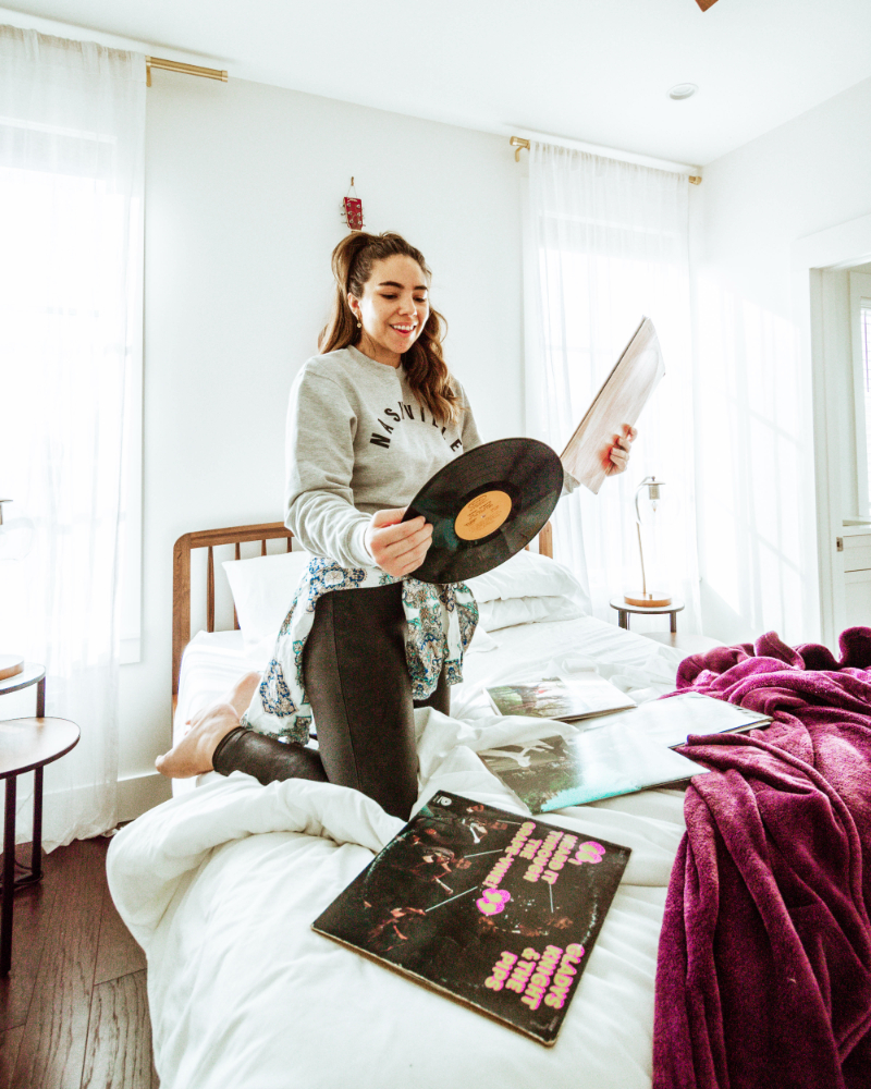 Lauryn Hock holding a record while kneeling on an unmade bed in Nashville, Tennessee