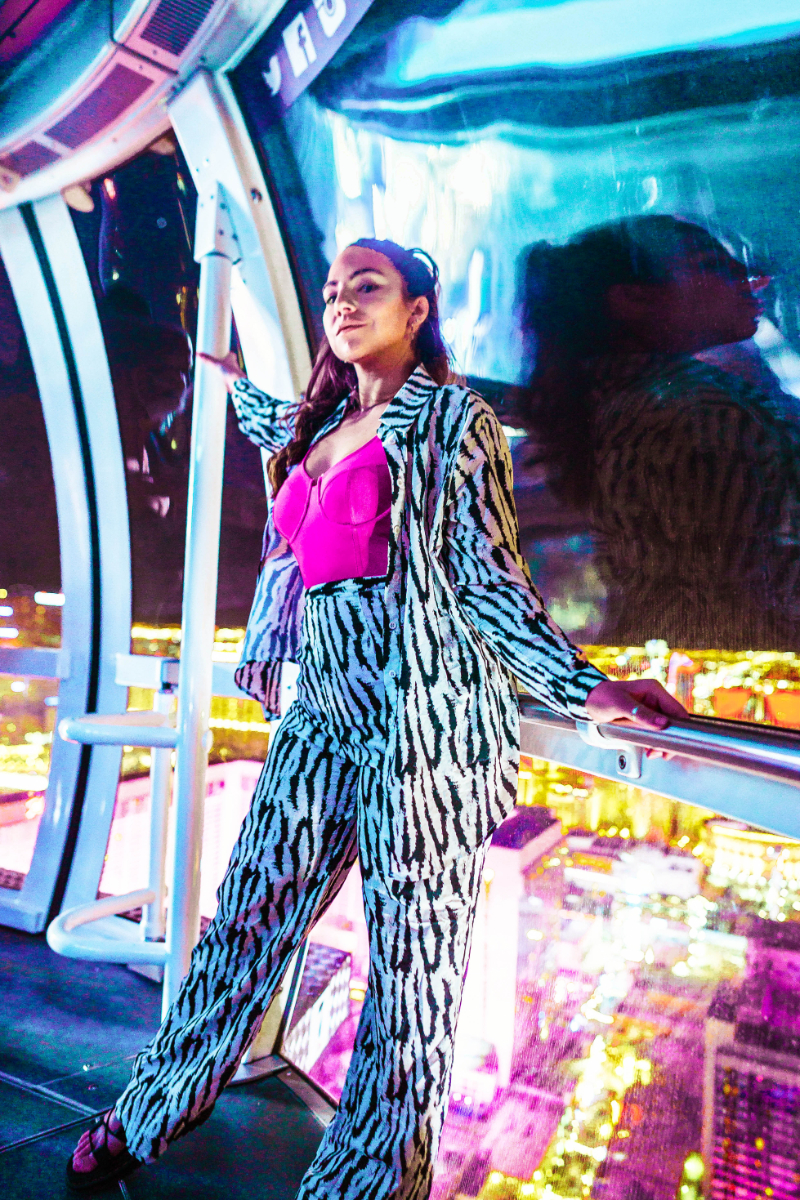 Nighttime on the Vegas High Roller showing the lit up city and The Strip below. Lauryn Hock, Travel blogger and beauty influencer, holds onto the railings of the observation pod while wearing a matching animal print set ootd
