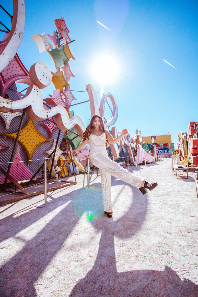 Vegas Neon Sign Museum during the day with fashion blogger Lauryn Hock kicking her leg in the air while wearing a white sequin jumpsuit in front of the Moulin Rouge sign