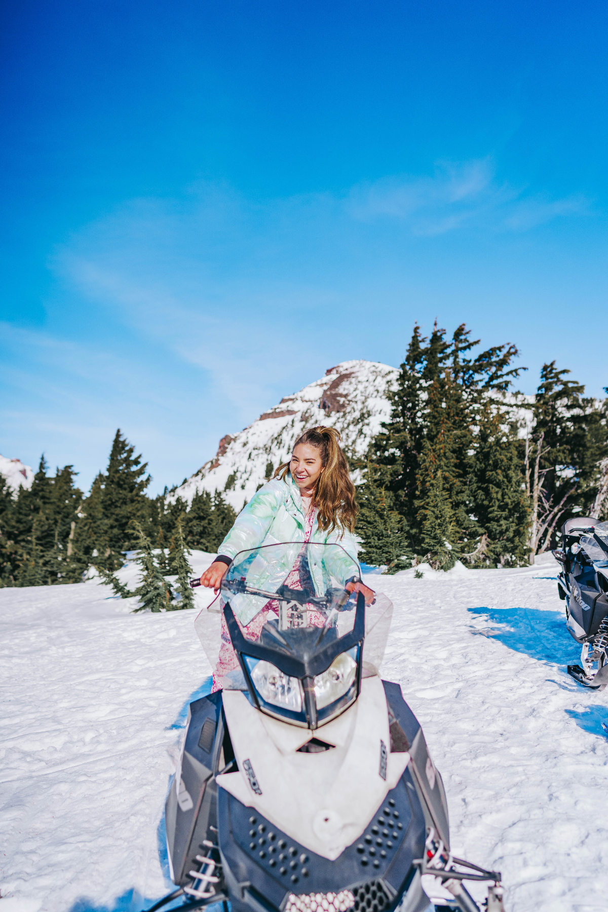 Things to do in bend Oregon: snowmobiling. Lauryncakes stands on a snowmobile in the middle of the Cascade Mountain range