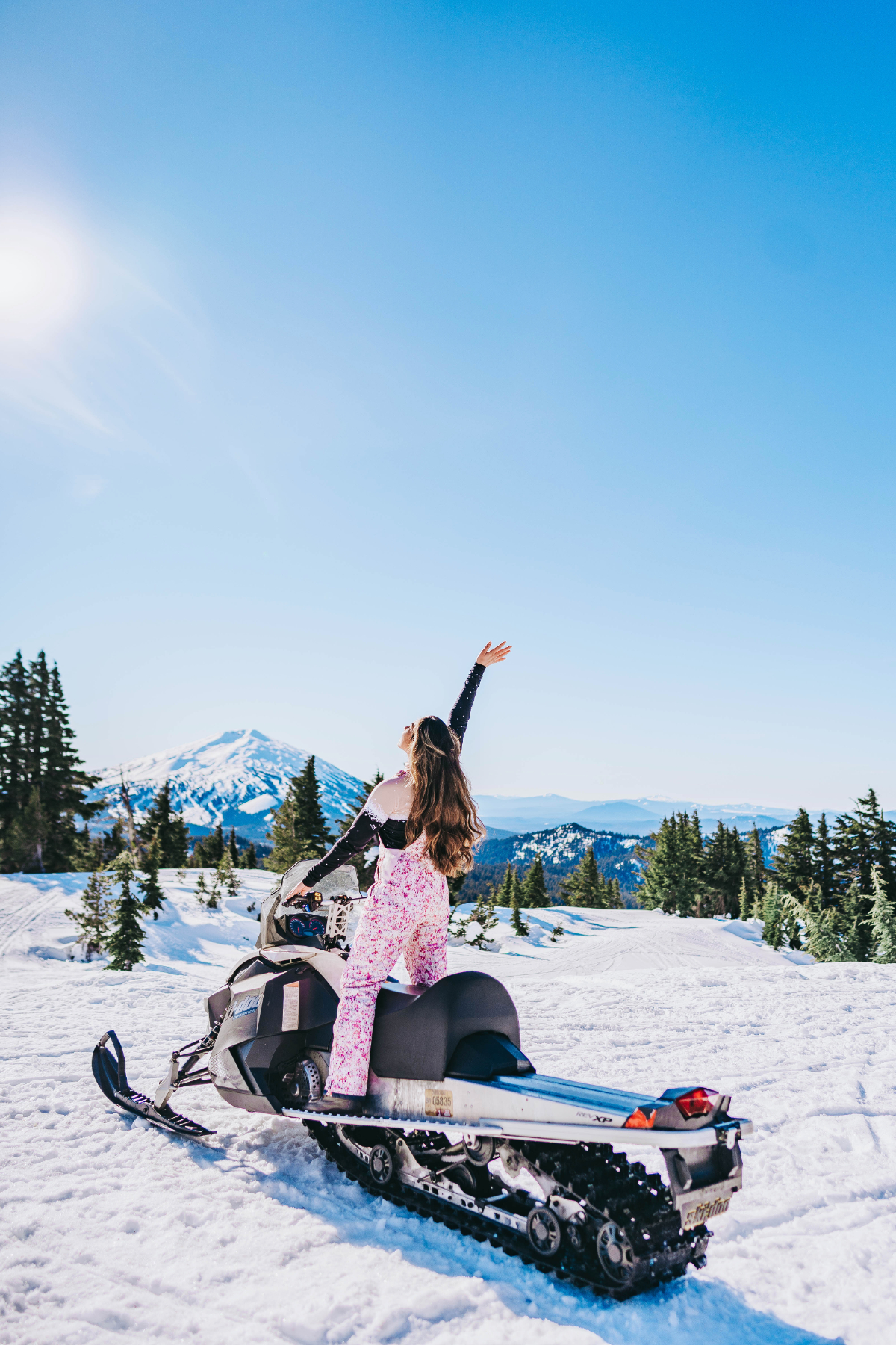 Woman with long brunette hair puts her hand up in the air as she does winter activities in Bend, Oregon