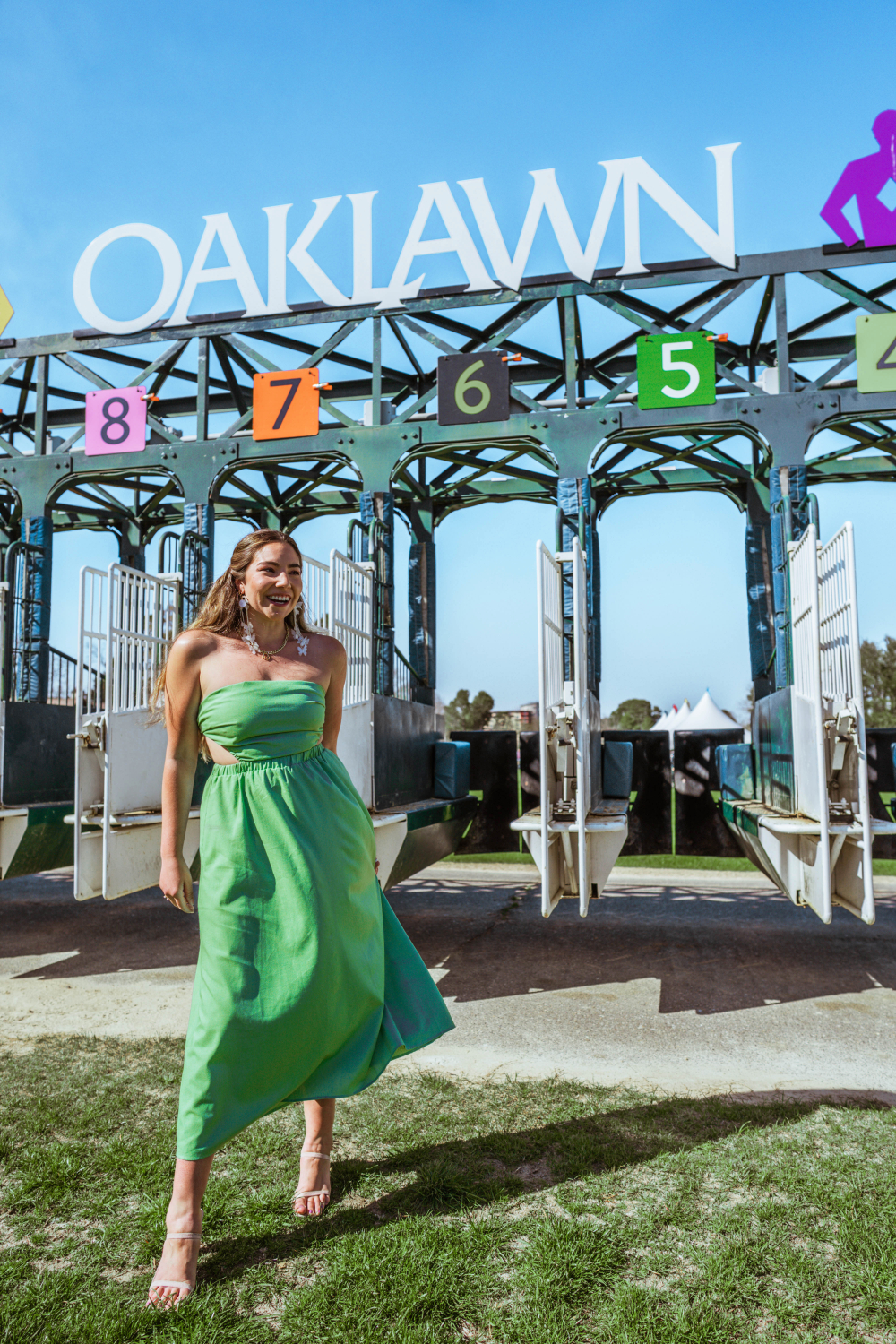 Fashion, beauty, and travel blogger Lauryn Hock in a green dress with cutouts at Oaklawn standing in front of the race gate