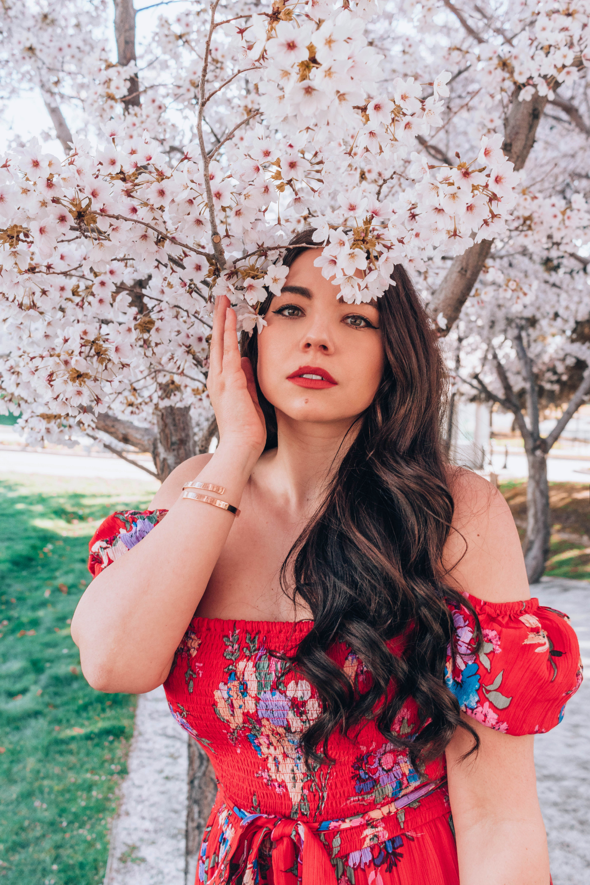 Lauryn Hock, style and travel blogger, has her hand near her face while standing under sakura cherry blossoms at the Utah State Capitol