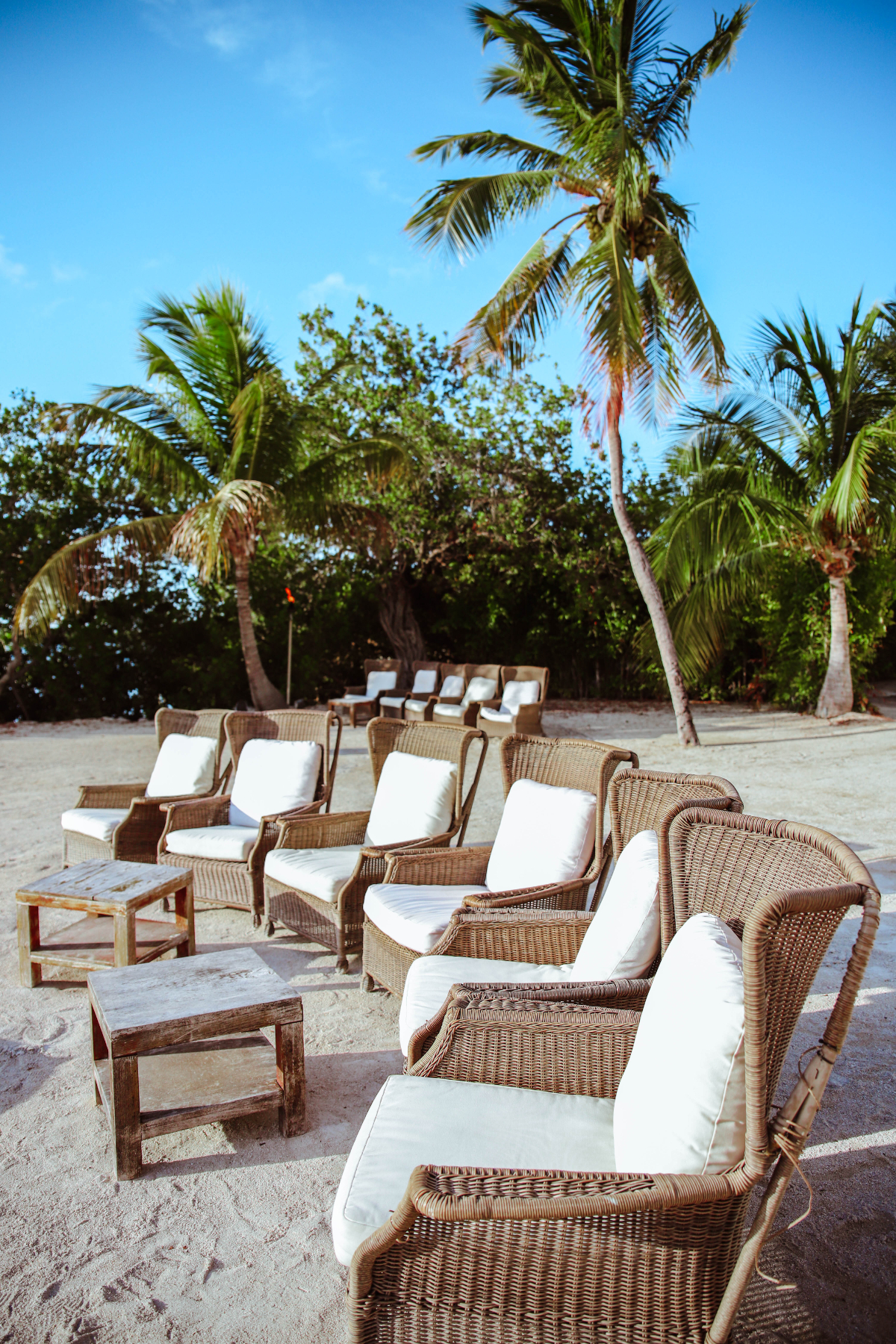 A Line of wicker beach chairs and tables are on the sand at Morada Bay Beach Cafe in the Florida Keys