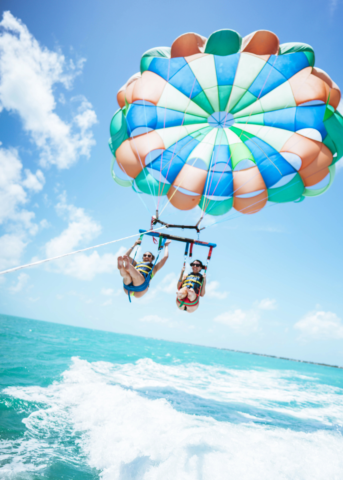 Two women laugh with their mouths open as they are strapped in to a parachute to go parasailing in Key West