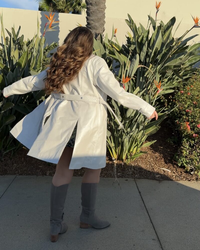 backside of a woman spinning wearing tall suede boots and a trench coat leather jacket