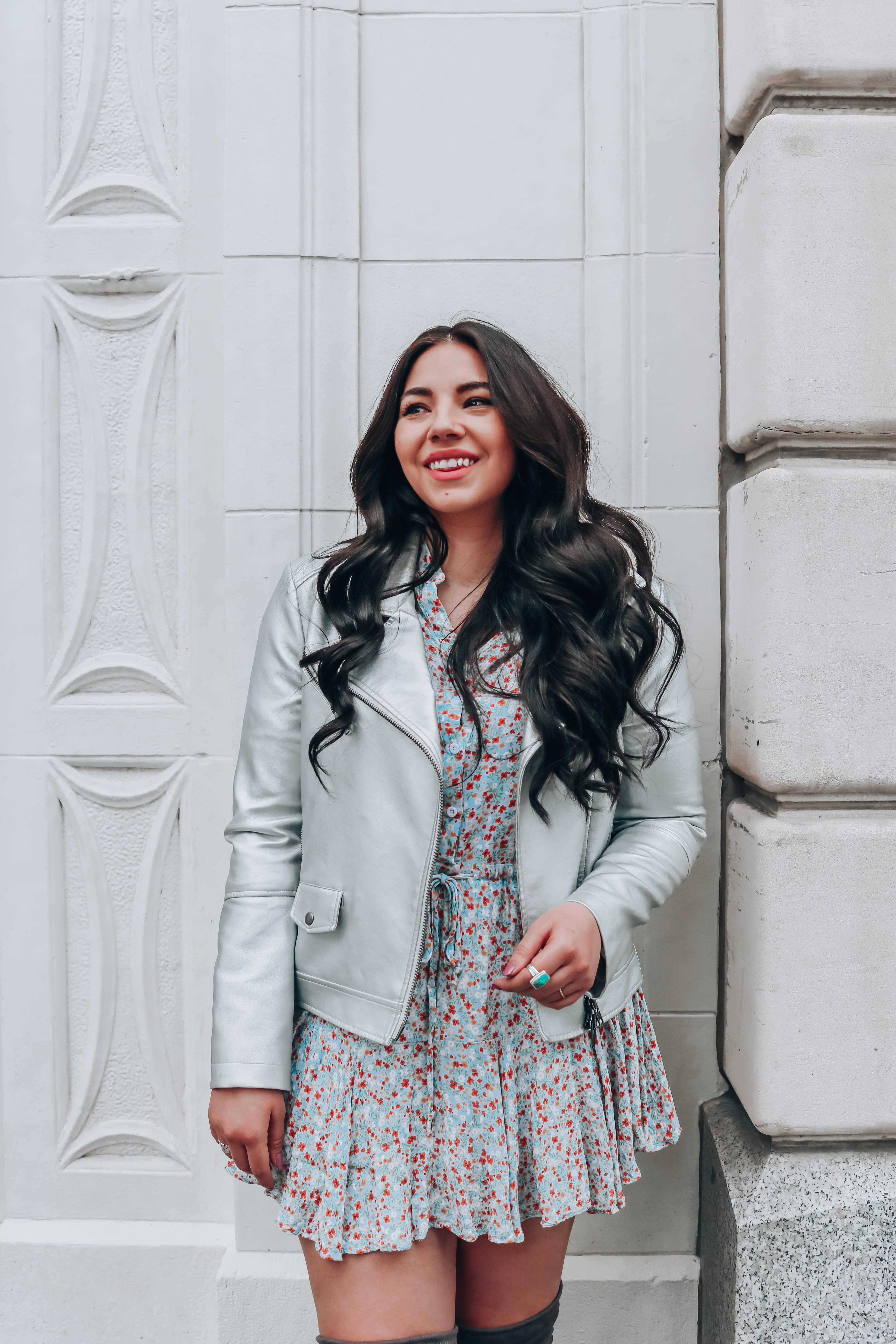 Lauryn Hock (brunette woman) laughing while leaning against a wall wearing a silver leather jacket and a mini skater dres